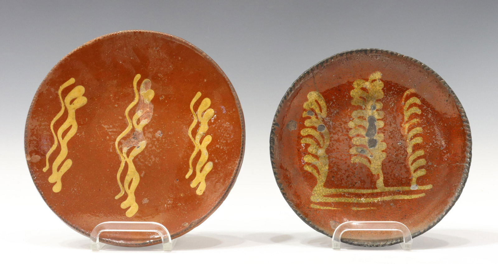(2) AMERICAN SLIP-DECORATED REDWARE POTTERY PLATES: (lot of 2) American slip-decorated redware pottery plates, Pennsylvania, 19th c., having a coggled rim, encircling linear yellow slip cup designs, unglazed bottom, expected rim and glaze chips, crazin