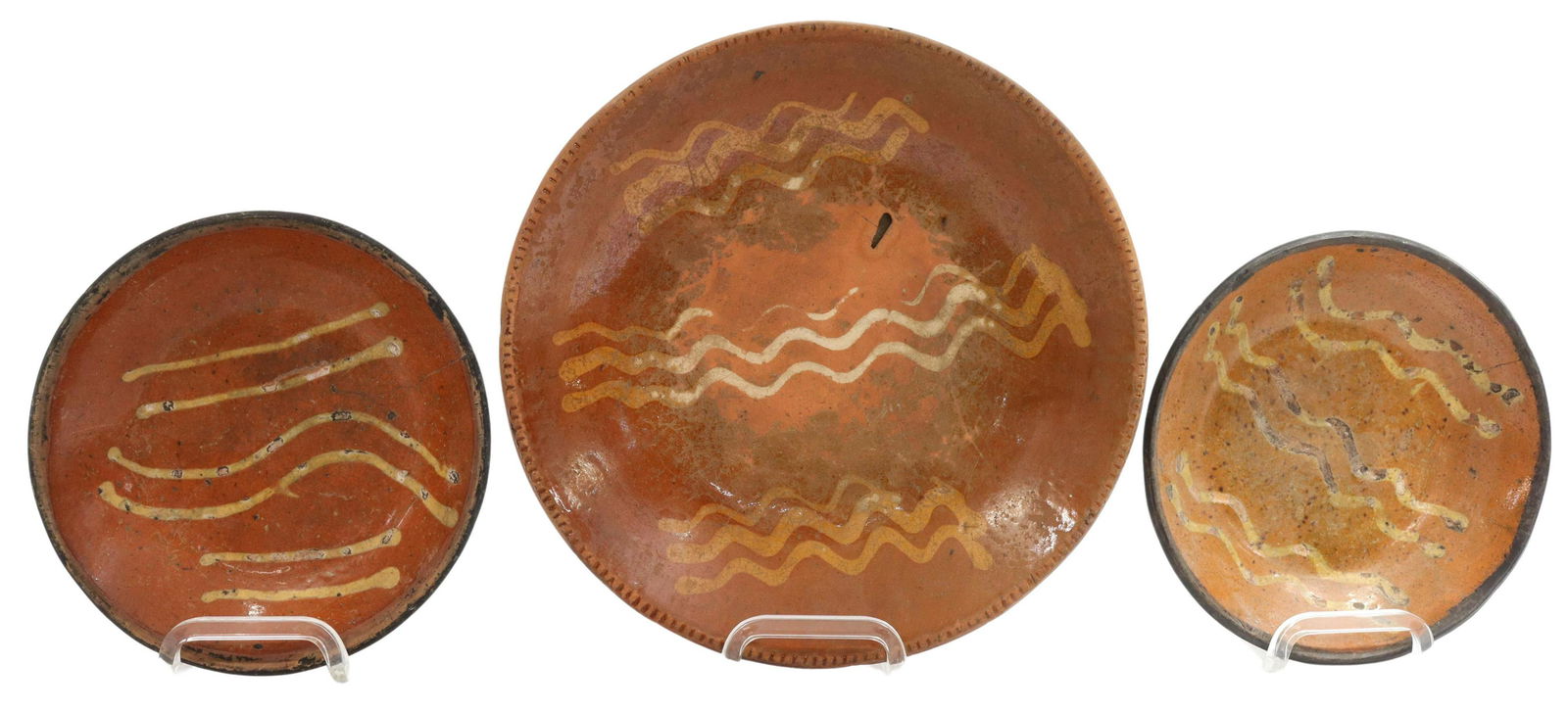 (3) AMERICAN SLIP-DECORATED REDWARE POTTERY PLATES: (lot of 3) American slip-decorated redware pottery plates, Pennsylvania and New England, 19th c., having plain and coggled rims, encircling linear yellow slip cup designs, unglazed bottom, expected ri