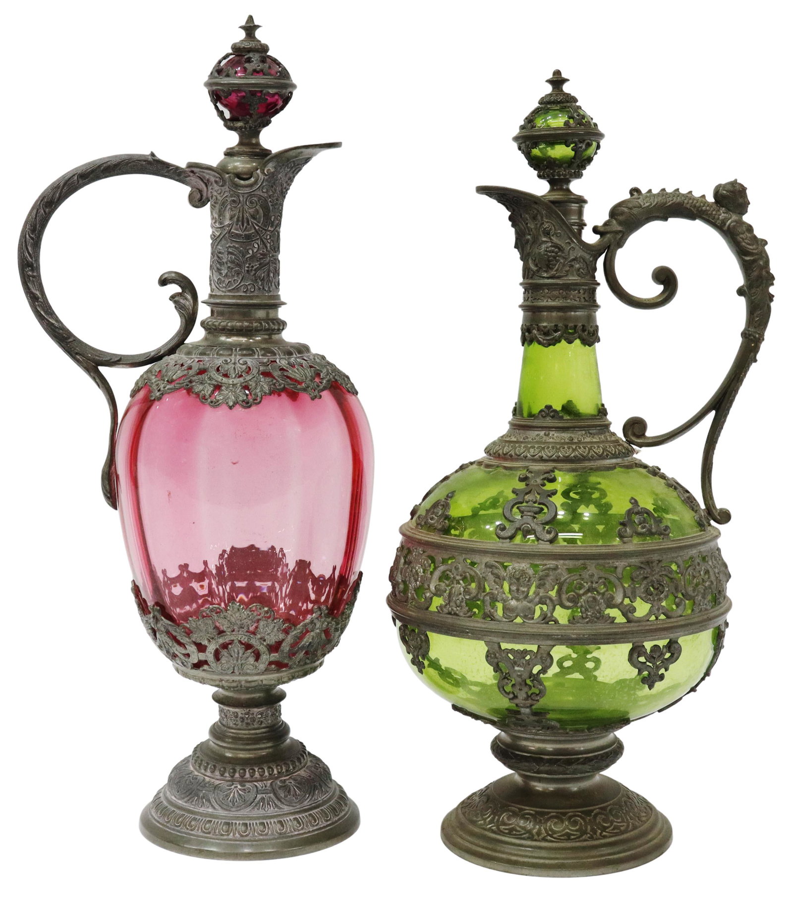 (2) PEWTER OVERLAY GLASS CLARET EWERS & STOPPERS: (lot of 2) Pewter-mounted glass claret ewers and stoppers, late 19th c., pewter vining foliate overlay, scrolled handle, (one) green, approx 13.5"h, 6"diam, (one) cranberry optic, approx 14.5"h, 4.75"