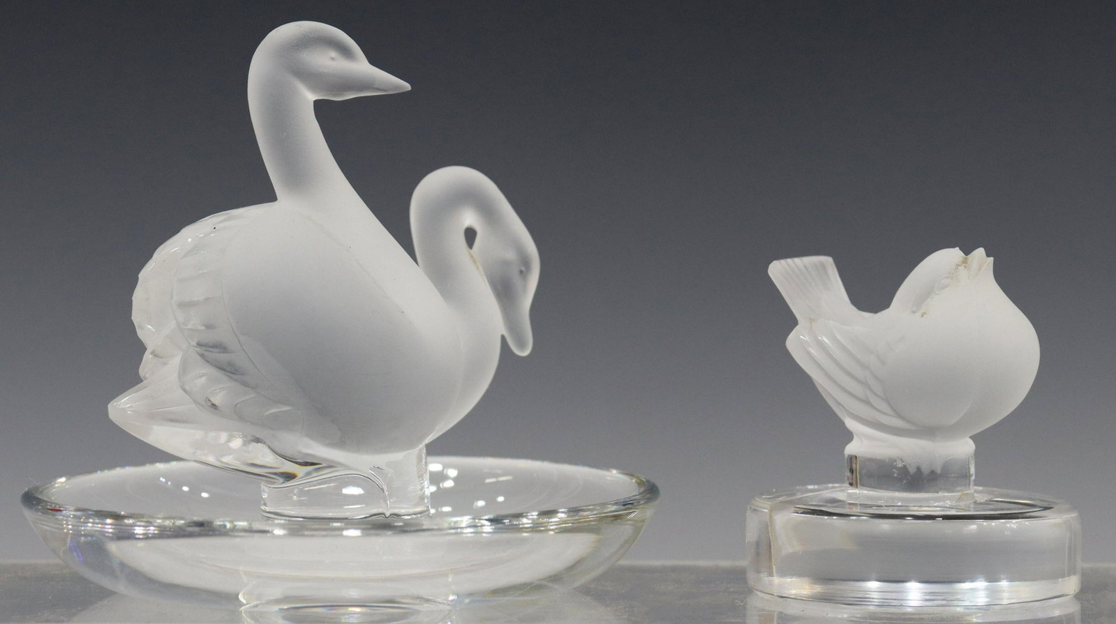 2) LALIQUE DEUX CYGNES PIN TRAY & PLACECARD HOLDER: (lot of 2) Lalique France art crystal table items, including: (1) finch place card holder, approx 2.25"h, 2"diam, (1) "Deux Cygnes" pin tray, with two satin-finish swans, approx 3.5"h, 4"diam; 1lbs to
