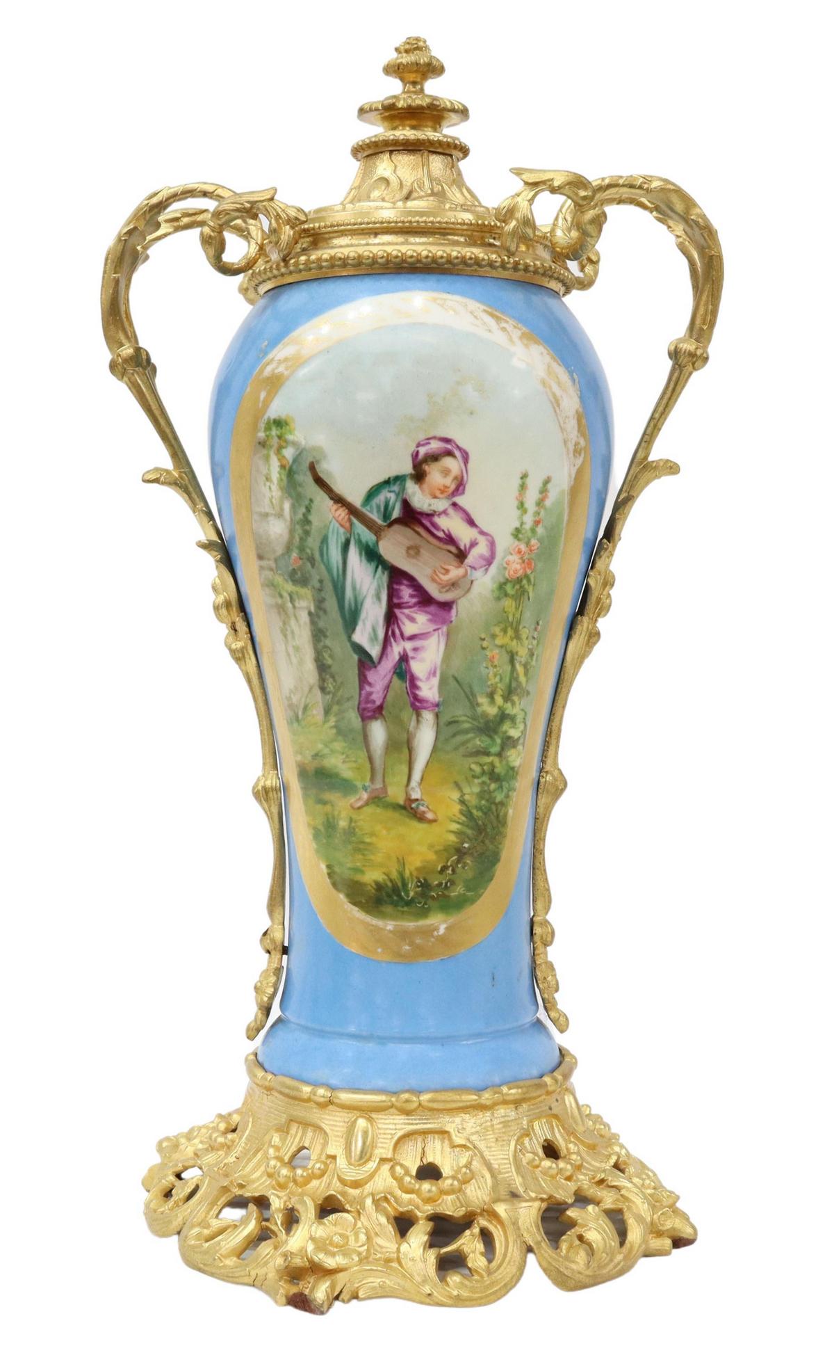 SEVRES STYLE METAL-MOUNTED PORCELAIN URN: Sevres style parcel gilt porcelain urn, 20th c., celeste bleu ground, having stationary lid with foliate and beaded accents, mounted scrolled handles, painted reserves with floral spray and musician p