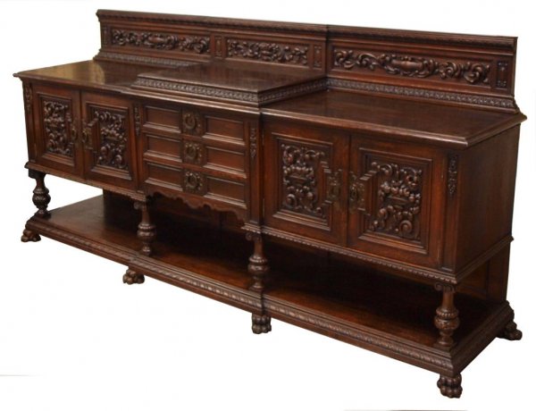 MONUMENTAL ANTIQUE SPAIN RELIEF CARVED OAK SERVER: Monumental Spanish oak server, early 20th c., profusely carved in relief with fruit and foliates, the ledge back surmounting the long case with stepped central section, double cabinet doors flank thre