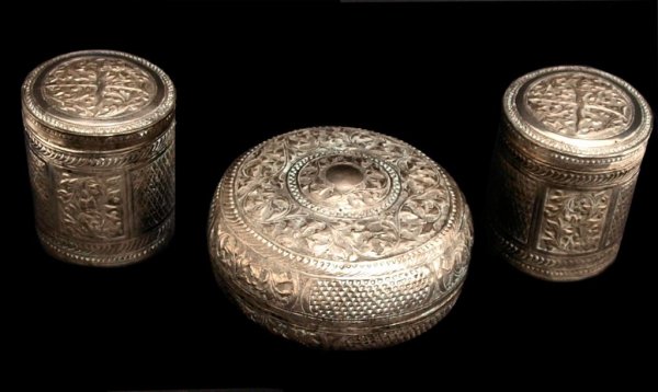 (3) SOUTHEAST ASIAN REPOUSSE SILVER LIDDED BOXES: (lot of 3) Southeast Asian lidded silver dresser boxes and jars, each with elaborate repousse vegetal and floral ornamentation, matching crossed keris and sheath emblem, (2) of cylindrical form, 3.5"h