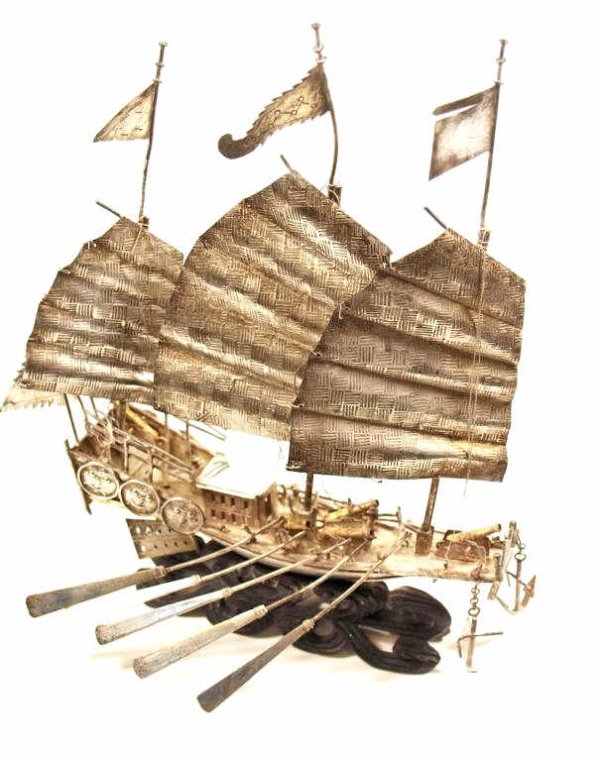 CHINESE MINIATURE SILVER CLIPPER SHIP WITH CANNONS: Chinese miniature silver boat with flags, cannons, oars, anchors, and figural medallions along side, the rear incised with characters, likely Southern China, mounted on a carved wave form base, some w