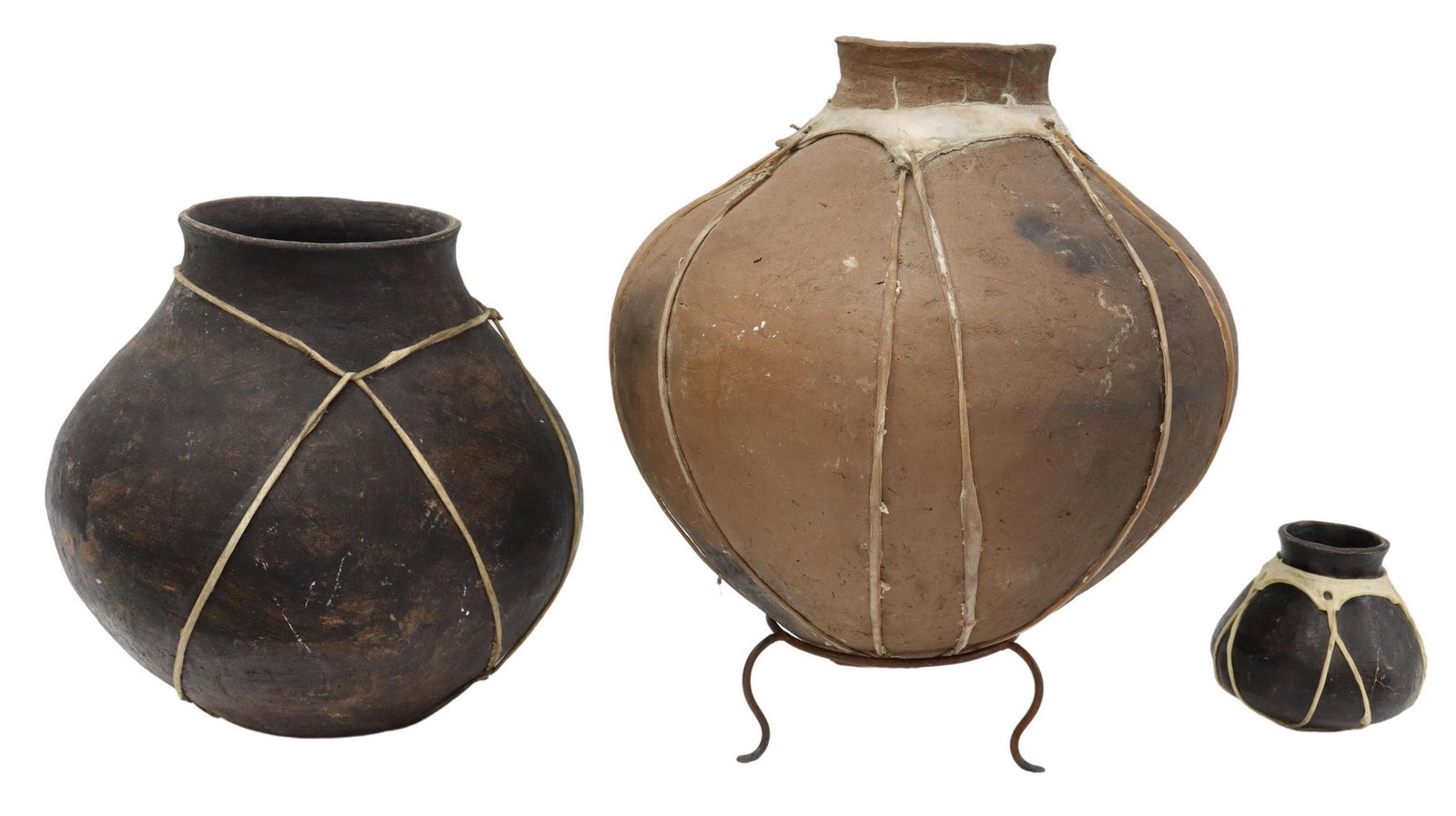 (3) PUEBLO STYLE POTTERY VESSELS: (lot of 3) Pueblo style pottery vessels, hand-formed, decorated with raw hide and sinew, comprising: (1) tapered form, decorated with faint hand print, presented on iron stand, approx 17.5"h, 17"diam;