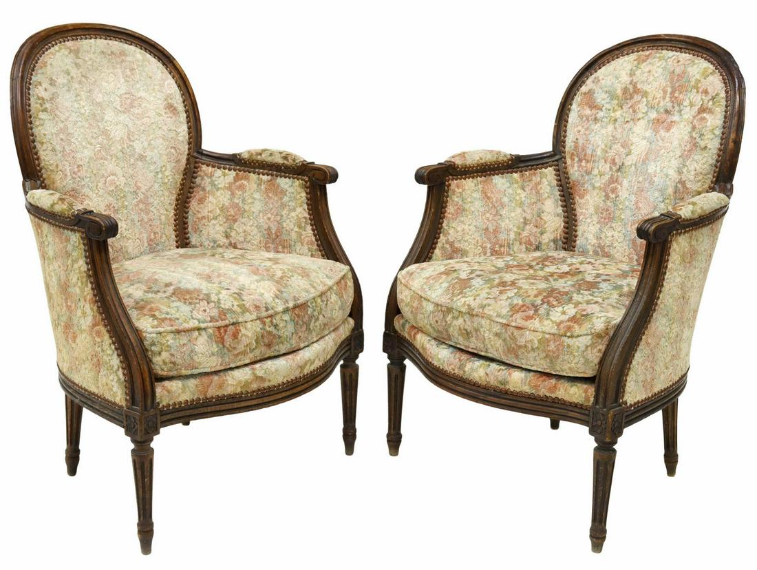 (2) FRENCH LOUIS XVI STYLE UPHOLSTERED BERGERES: (pair) French Louis XVI style armchairs, early 20th c., curved walnut frame, closed arms, scrolled handholds, floral upholstery, with nailhead trim, loose seat cushion, carved floral medallions, risin