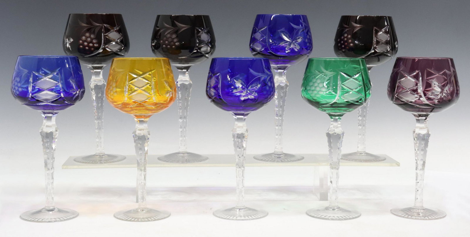 (8) BOHEMIAN CUT-TO-CLEAR GLASS WINE STEMS: (lot of 9) Bohemian cut-to-clear glass wine goblets, bowls cut with grape clusters, hatch-patterned diamonds, tapered notched stem, on a cut foot, including: (1) green, (1) amber, (1) amethyst, (3) co