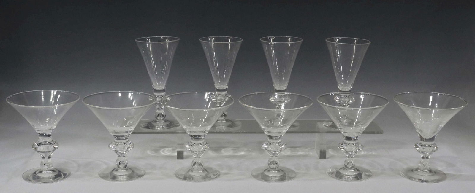 (10) STEUBEN ART GLASS TRUMPET 7737 STEMWARE: (lot of 10) Steuben "Trumpet" colorless art glass stemware, 20th c., pattern number 7737, each with engraved signature underfoot, comprising: (6) champagne/ tall sherbet glasses, approx 5"h, 4.5"diam;