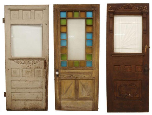 (3) ARCHITECTURAL STAINED GLASS & OTHER WOOD DOORS: (lot of 3) Architectural wood doors including: (1) with a surround of blue, green and yellow textured stained glass squares centering a floral etched panel, remnants of paint to paneled door, 82"h, 34
