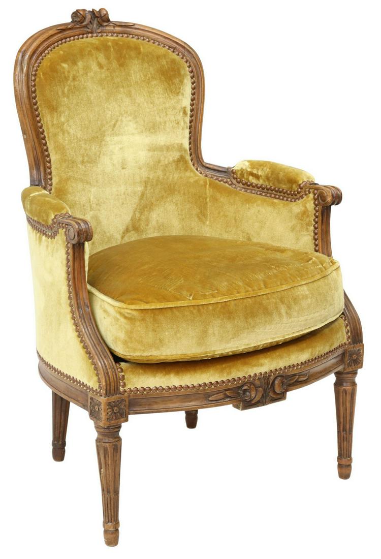 FRENCH LOUIS XVI STYLE UPHOLSTERED BERGERE: French Louis XVI style armchair, 20th c., walnut frame, velvet upholstery with nailhead trim, closed arms, scrolled handholds, loose seat cushion, carved floral medallions over fluted tapered legs, en
