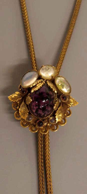 VICTORIAN SLIDE NECKLACE AMETHYST COLOR CABOCHONS: Victorian slide necklace, the long braided chain ending in tassels, ornate slide having a leafy foliate frame set with opalescent and small amethyst cabochons, large central amethyst color cabochon wi