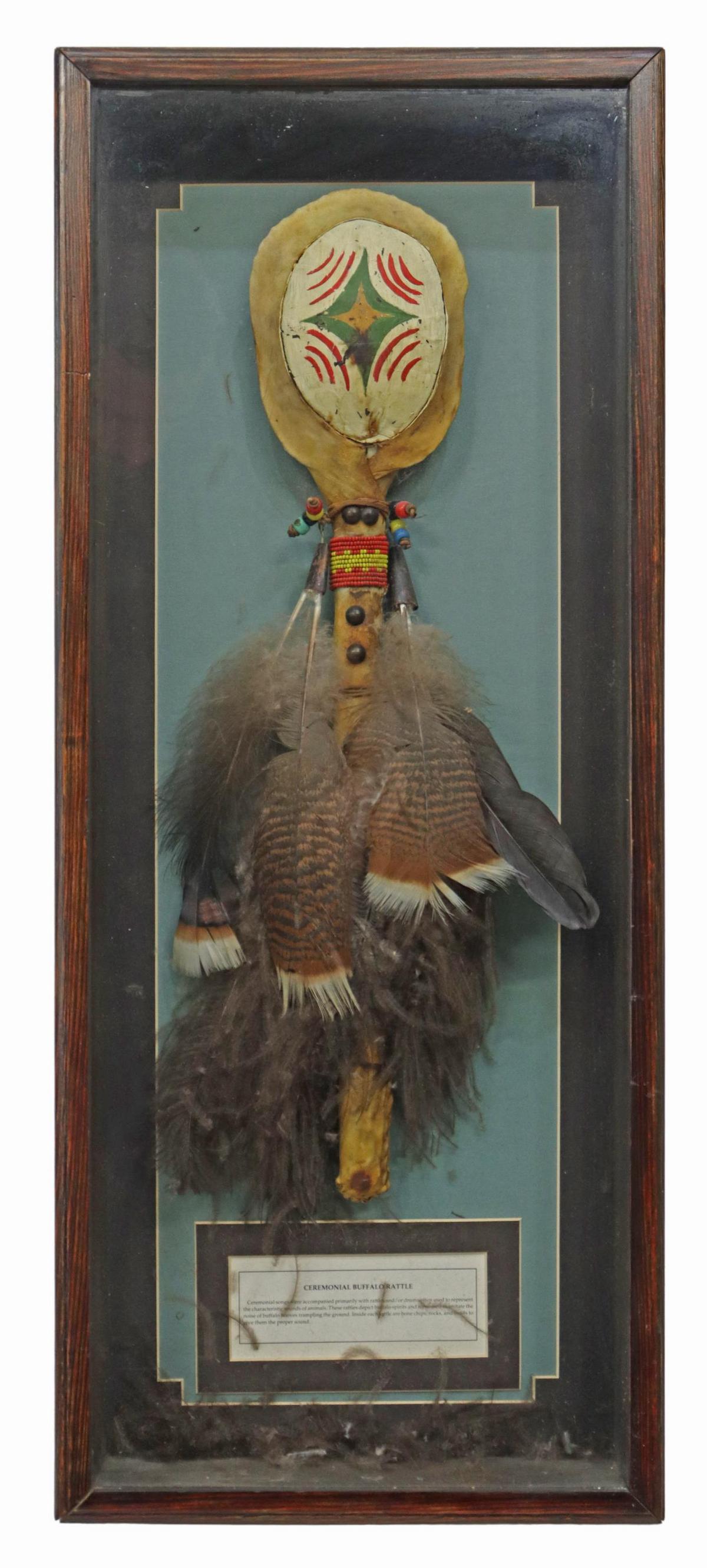 SHADOWBOX FACSIMILE NATIVE AMERICAN BUFFALO RATTLE: Native American style replica ceremonial buffalo rattle, painted hide, with bead work, feathers, housed in a shadowbox frame, rattle: approx 19.5"l, overall: 29.25"h, 12.25"w Start Price: $60.00