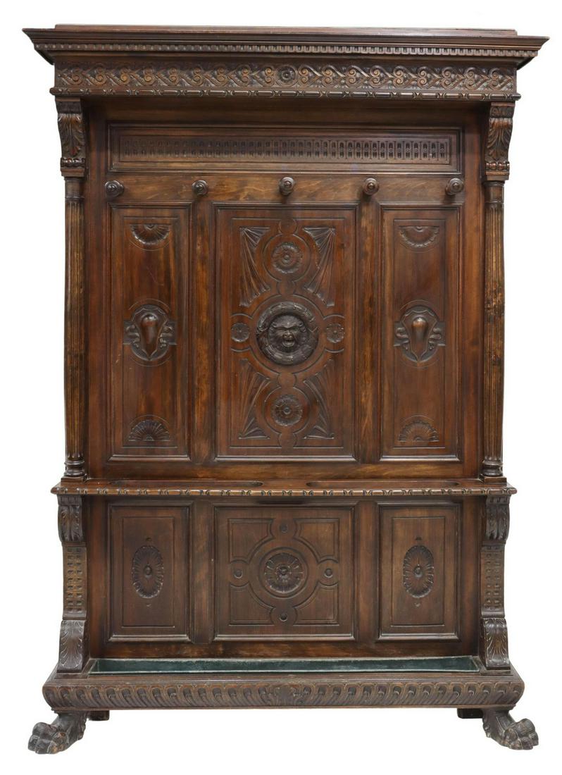 ITALIAN RENAISSANCE REVIVAL WALNUT HALL TREE: Italian Renaissance Revival walnut hall tree, early 20th c., accented by carved ornamental moldings, five turned hooks, central mask and floral motifs, umbrella rail over lower drip tray, terminating 