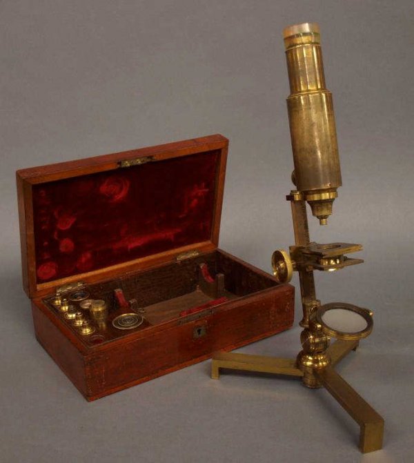 VICTORIAN CASED BRASS STUDENTS MICROSCOPE: Victorian brass students microscope raised on a graduated swiveling tri-foot, accompanied by many accessories and presented in the original fitted, flame mahogany box with inset brass cartouche, retai