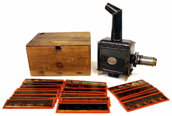 ERNST PLANK MAGIC LANTERN & 23 COLOR SLIDES: (lot) Magic lantern projector, Ernst Plank, Germany, c. 1900, with glass chimney, lens, reflector, lacking burner and collar, accompanied by twenty three (23) glass, color slides, in a dovetailed wood