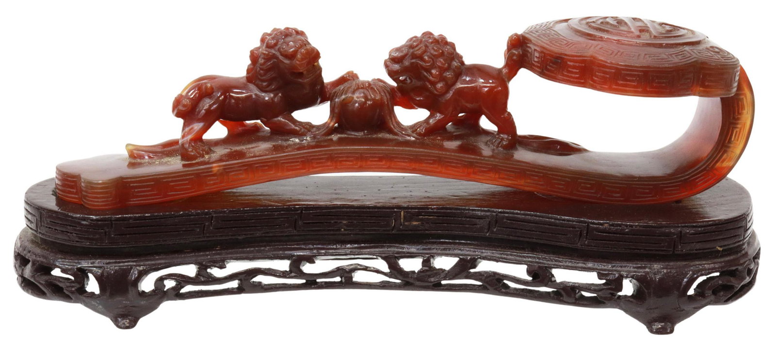 CHINESE CARVED CARNELIAN RUYI SCEPTER ON STAND: Chinese carved carnelian agate ruyi scepter, with Greek key border, Shou symbol, opposing foo lions with their paws on a ball, accompanied by wood stand, approx 4"h, 10.25"l, 3.5"w (on stand); 1.25lbs