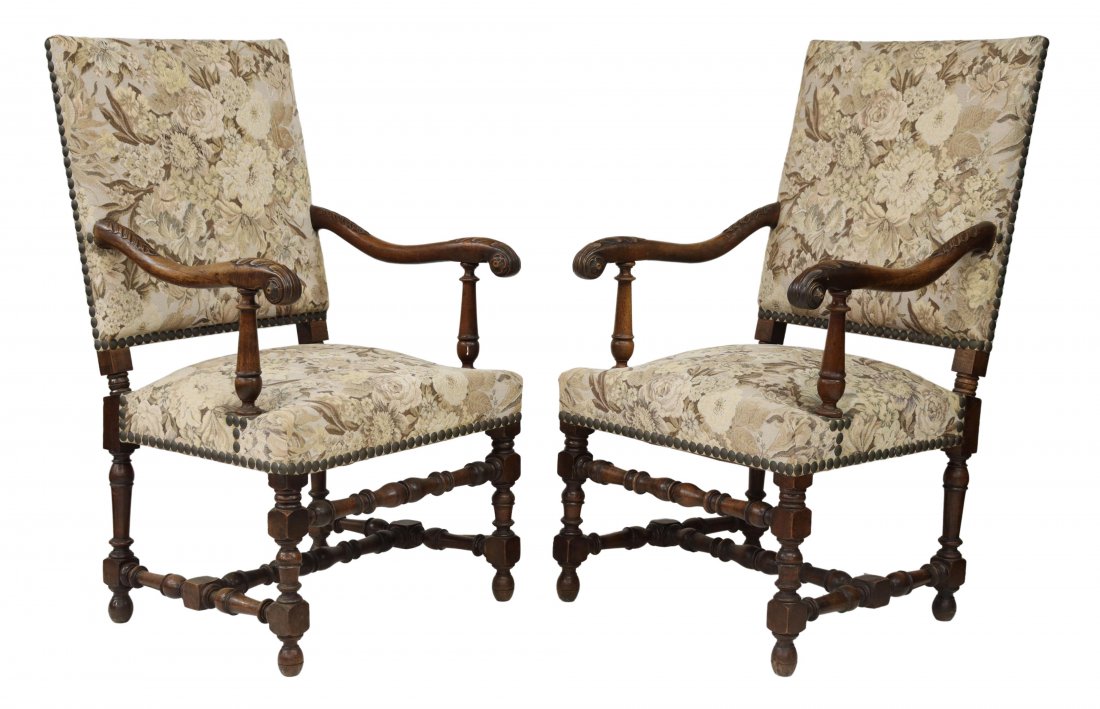(2) FRENCH LOUIS XIII STYLE CARVED WALNUT FAUTEILS: (pair) French Louis XIII style walnut highback armchairs, late 19th c., large nail head trim, woven floral upholstery, each frame with carved curving arms, ending in scrolled hand holds, rising on blo