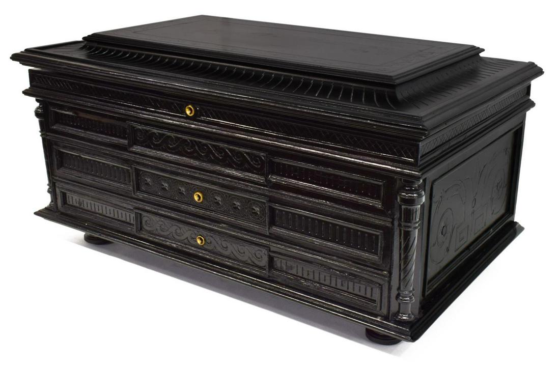 EBONIZED SILVER CHEST OR JEWEL CASKET: Silver chest or jewel casket, ebonized case with incised foliate carving, the hinged top opening to a lift-out tray, two lower exterior lockable drawers, molded base further raised on bun feet, approx