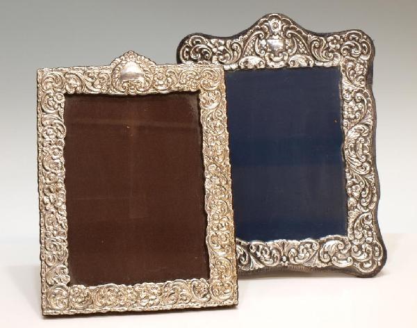 (2) STERLING SILVER REPOUSSE PICTURE FRAMES: (lot of 2) Sterling silver repousse frames:(1) English frame having profuse repousse scroll and floral decoration, blue velvet backing, hallmarked with RC, flower, lion passant, N, 10.75"h, 8.5"w; (1)