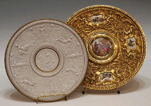 GILT METAL & PORCELAIN WALL PLAQUES IN RELEIF: (lot of 2) Gilded metal wall plaque, profusely decorated in relief with winged cherubs, porcelain reserves transfer decorated with a courting scene and scantily clad cherubs, 10.5"diam; together with 