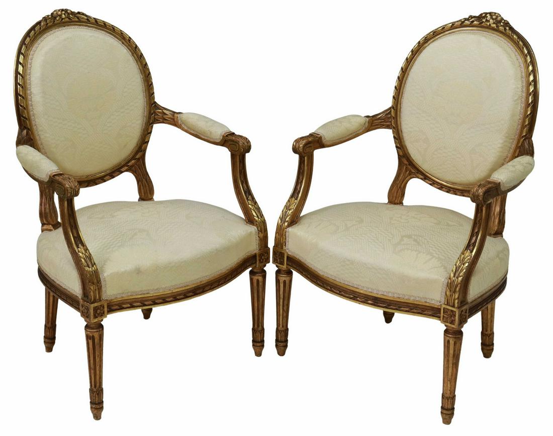 (2) LOUIS XVI STYLE GILTWOOD OVAL BACK FAUTEUILS: (pair) French Louis XVI style giltwood armchairs, early 20th c., floral crest, medallion back with ribbon twist molding, padded arms ending in acanthus scroll handholds, upholstered seat, rising on ta