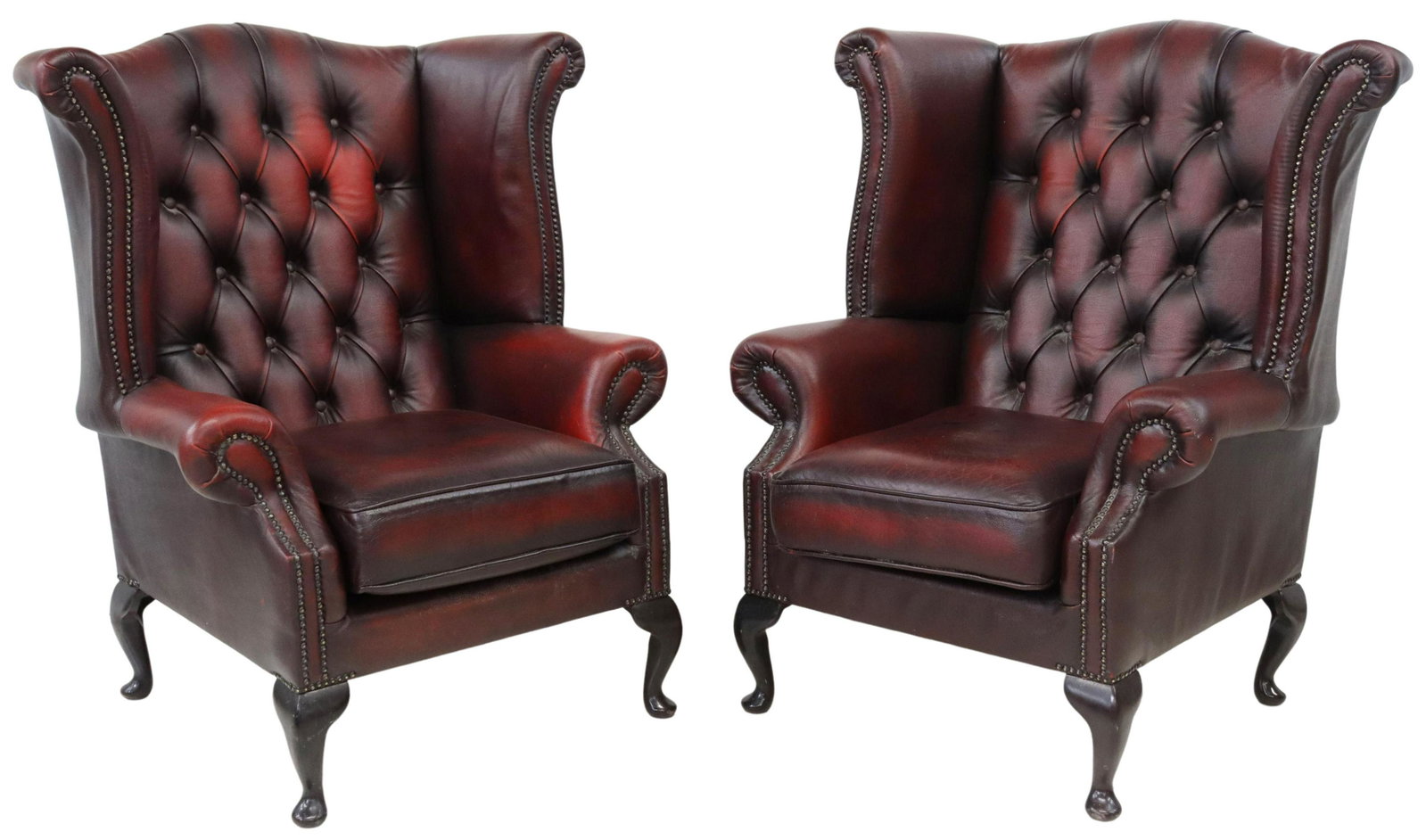 (2) QUEEN ANNE STYLE OXBLOOD WINGBACK ARMCHAIRS: (pair) Queen Anne Style wingback armchairs, late 20th c., in oxblood leather upholstery, with button-tufted back, rolled arms, loose seat cushion, nail head trim, rising on cabriole legs, ending in pa