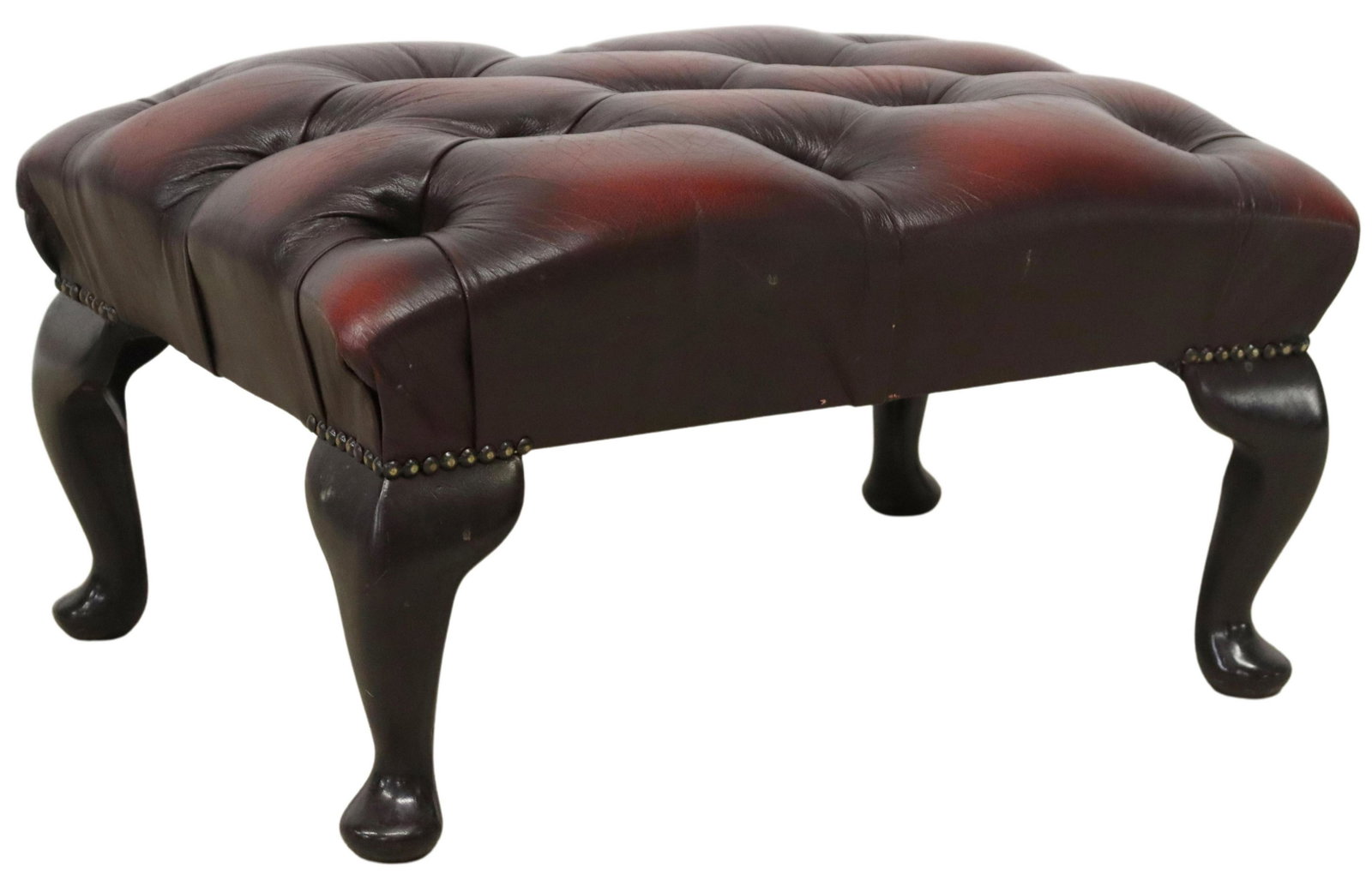 QUEEN ANNE STYLE OXBLOOD LEATHER OTTOMAN/ STOOL: English Queen Anne style footstool/ottoman, late 20th c., in oxblood leather upholstery, with button-tufted seat, brass tack trim, rising on ebonized cabriole legs, ending in pad feet, approx 12.5"h, 
