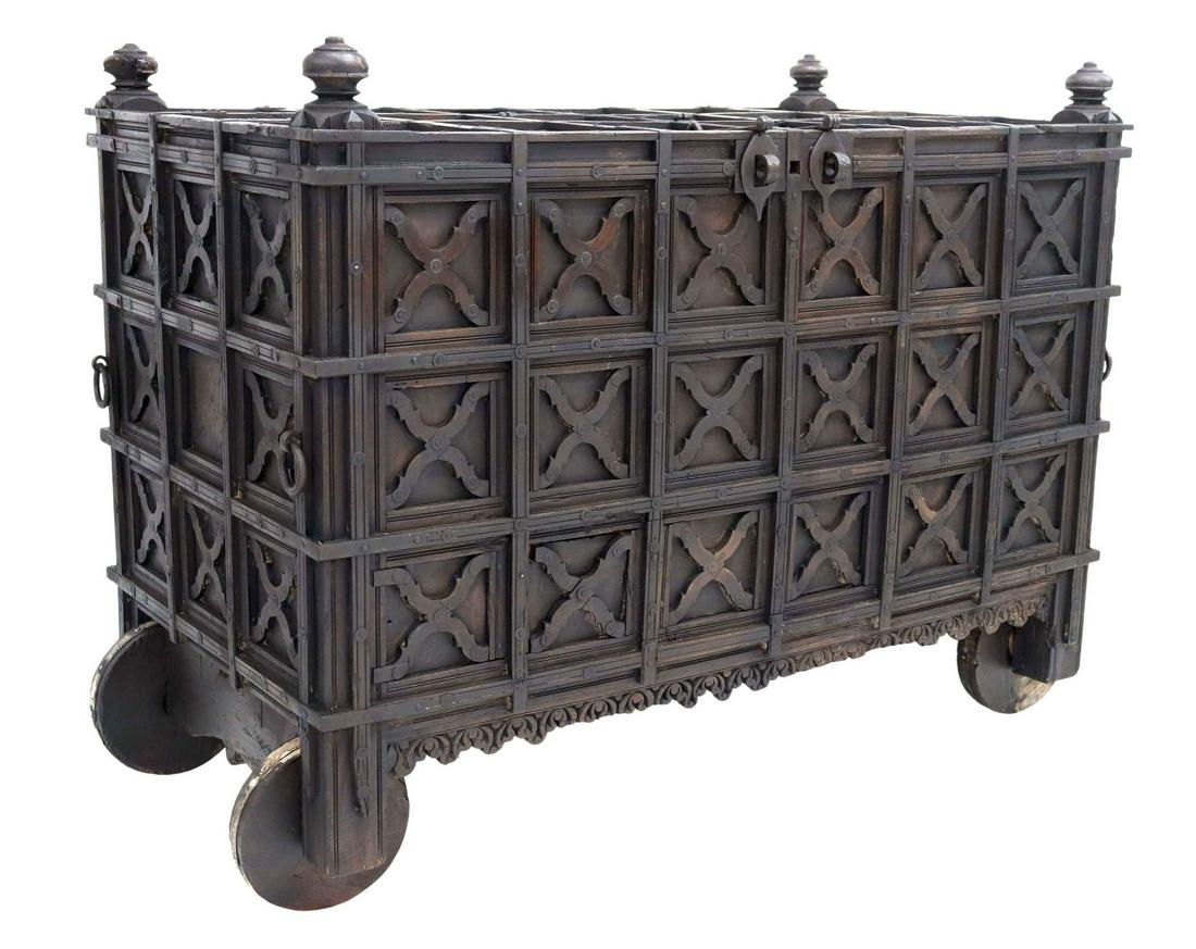 IRON-STRAPPED TEAKWOOD DOWRY CHEST, INDIA: Large metal-bound teakwood dowry chest, India, 19th c., turned finials, hinged top with iron hasp, open interior, paneled sides with x-form decorative elements, carved apron, on wooden wheels, approx 