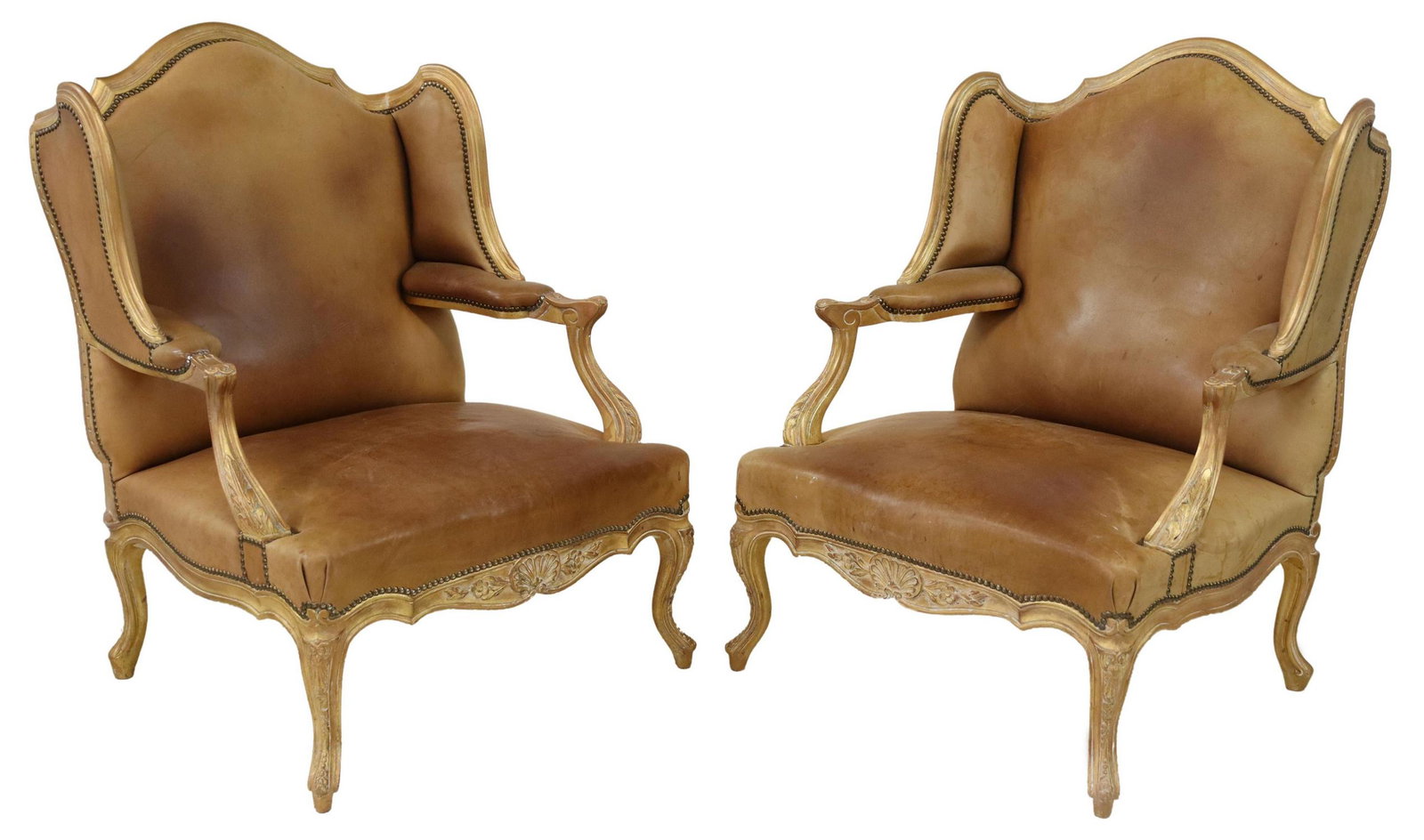 (2) LOUIS XV STYLE GILTWOOD WINGBACK BERGERES: (pair) Louis XV style giltwood wingback armchairs, 20th c., carved foliate and shell frame, upholstered in tan leather, with nailhead trim, rising on cabriole legs, approx 42"h, 30.5"w, 26"d, seat hei