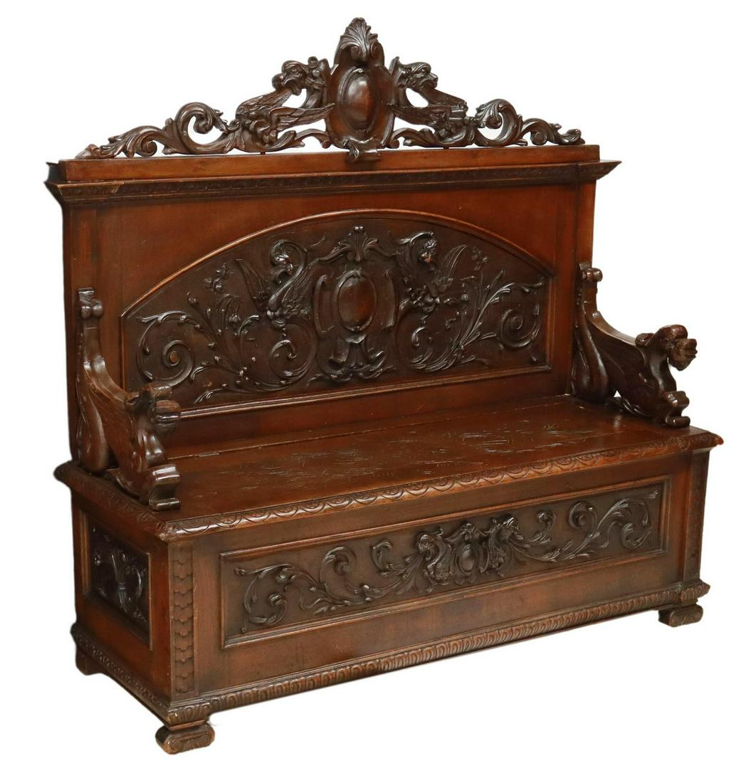 ITALIAN RENAISSANCE REVIVAL CARVED HALL BENCH: Italian Renaissance Revival walnut hall bench, late 19th c., having carved crest over high back, hinged bench seat with incised foliates, flanked on both sides by carved griffin armrests, with foliate