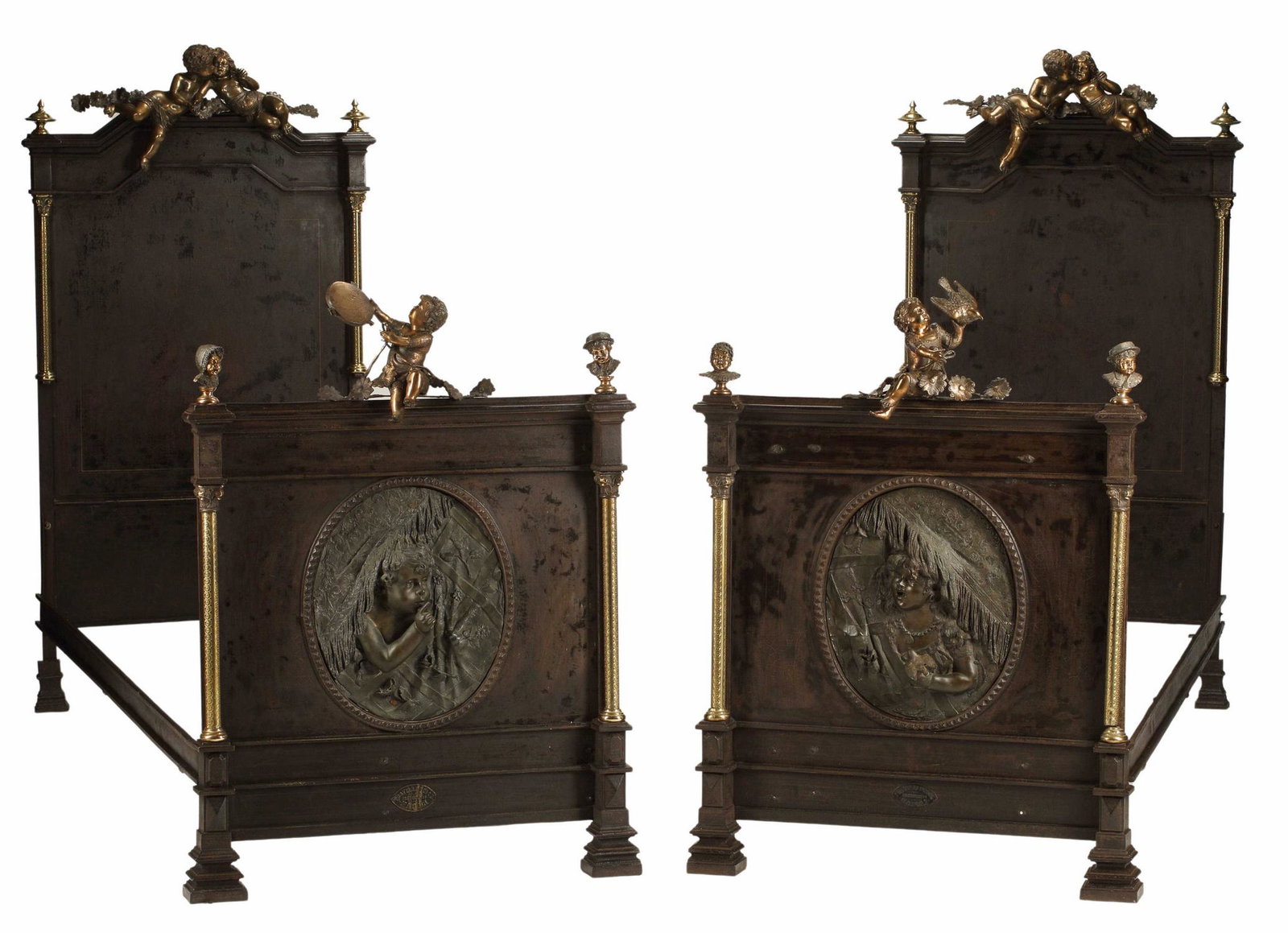 (2) EXCEPTIONAL IRON & BRONZE PUTTI MOUNTED BEDS: (pair) Exceptional bronze mounted iron beds, crested by large robust draped putti and flowers, gilt metal finials and corinthian columns to each side, each footboard further mounted with figural bust 