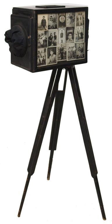 VINTAGE MOROCCAN BOX CAMERA ON TRIPOD STAND: Vintage Moroccan bellows camera, c. 1920's, the box lined with vintage photos on either side, H. Roussel , Paris, Stylor 14.5 lens, raised on a tripod base, 57"h, 22"w, 11"d, 30lbs total Start Price: