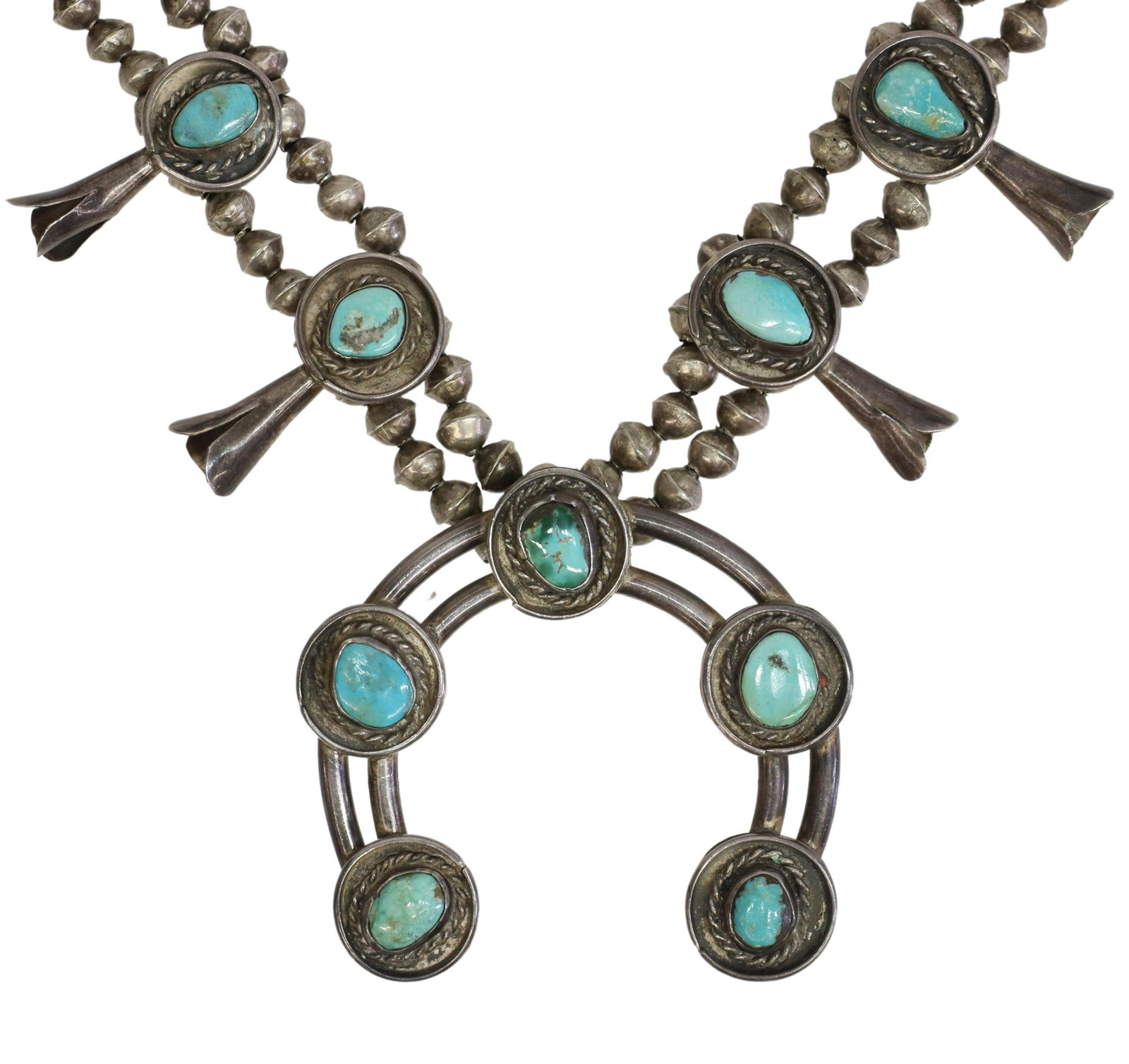 NATIVE AMERICAN TURQUOISE SQUASH BLOSSOM NECKLACE: Native American silver (content unknown) squash blossom necklace, ten blossoms, each set with a turquoise cabochon, twisted wire rope border, central naja pendant, double bench bead strands, ending in