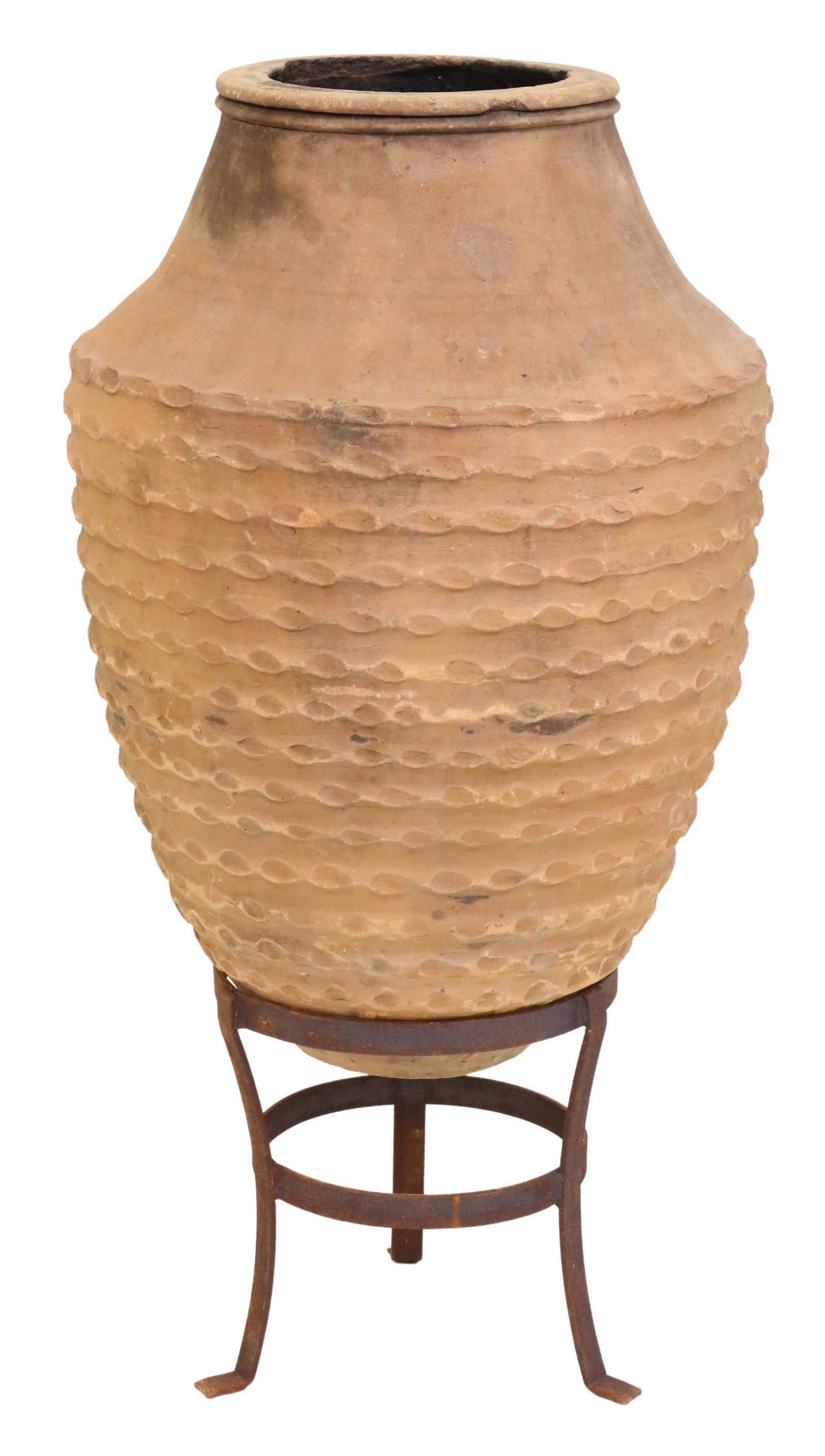 LARGE BANDED TERRACOTTA OLIVE JAR IN IRON STAND: Large terracotta olive jar, early 20th c., wide rim, over tapered and banded body, resting in iron tripartite base, black marks from firing, approx 39"h, 21"diam Start Price: $200.00
