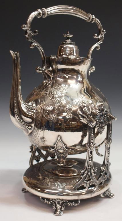 ORNATE SILVER PLATE TILTING TEA KETTLE ON STAND: Silver plate tilting tea kettle on conforming stand with warmer lacking handle, decorated with floral engraving, the kettle marked with a crown and numerals within a diamond, kettle: 11.75"h, 9"w, 9.5