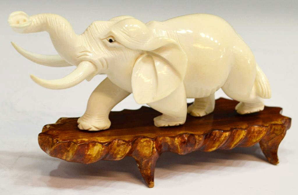 CHINESE CARVED IVORY ELEPHANT ON HARDWOOD BASE: **This item will not be shipped Internationally** Carved running ivory elephant with trunk and tusks extended, rising on hardwood stand, light fissures near tail, elephant: 2.5"h, 6"w, 2"w, stand: 1.1