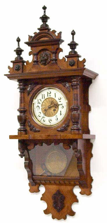 ANTIQUE GERMAN CARVED WALNUT WALL CLOCK: German walnut wall clock, possibly Kienzle, late 19th c., the front with foliate carving and lion head, columns flanking a glass door, allowing access to the porcelain dial with Roman numerals, time a