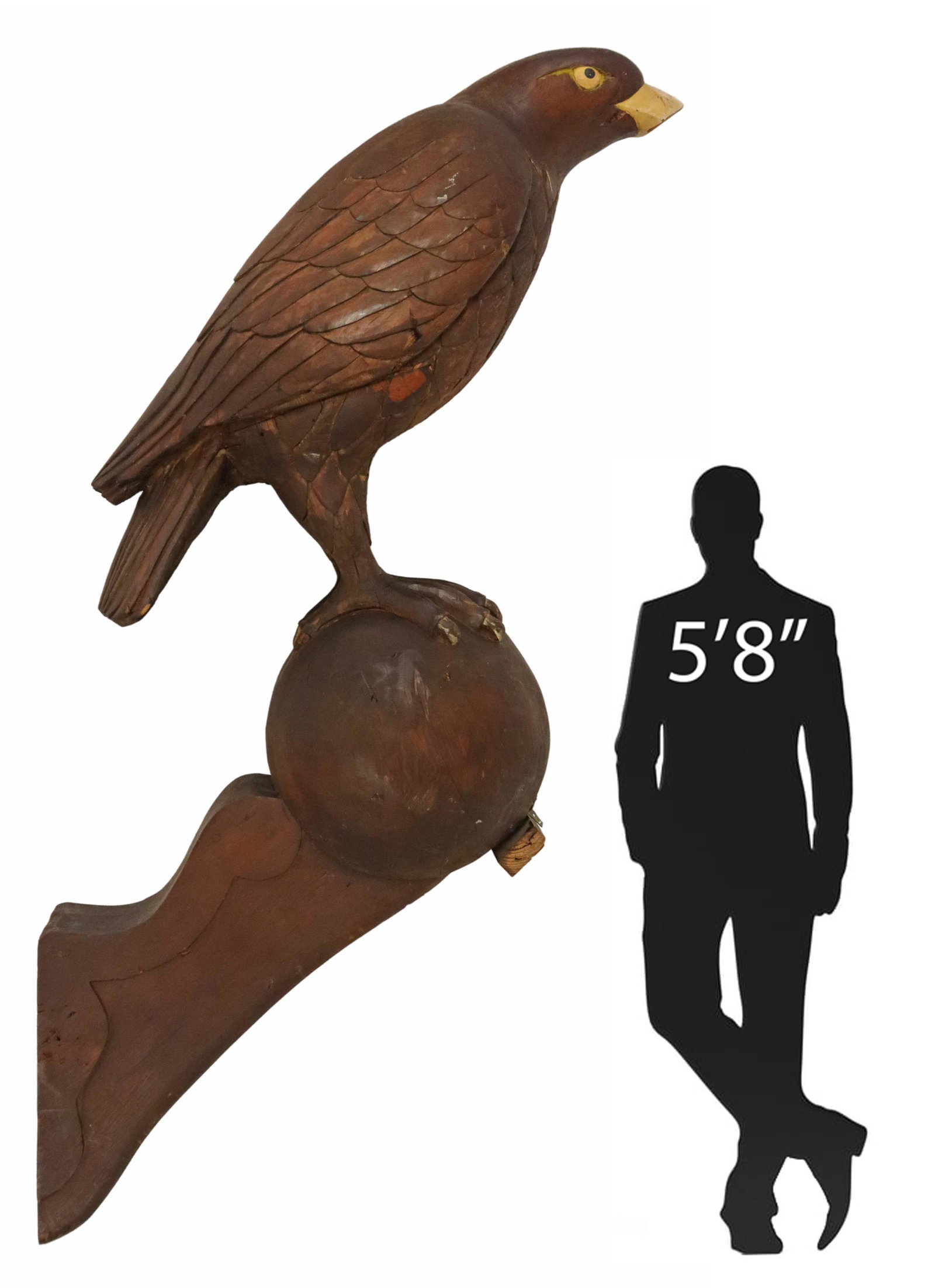 CARVED WOOD EAGLE ON BALL ARCHITECTURAL ELEMENT: Architectural carved wood sculptural element, in the form of an eagle, with yellow painted beak and eyes, having closed wings, perched on a ball, mounted to scalloped bracket, not freestanding, some l