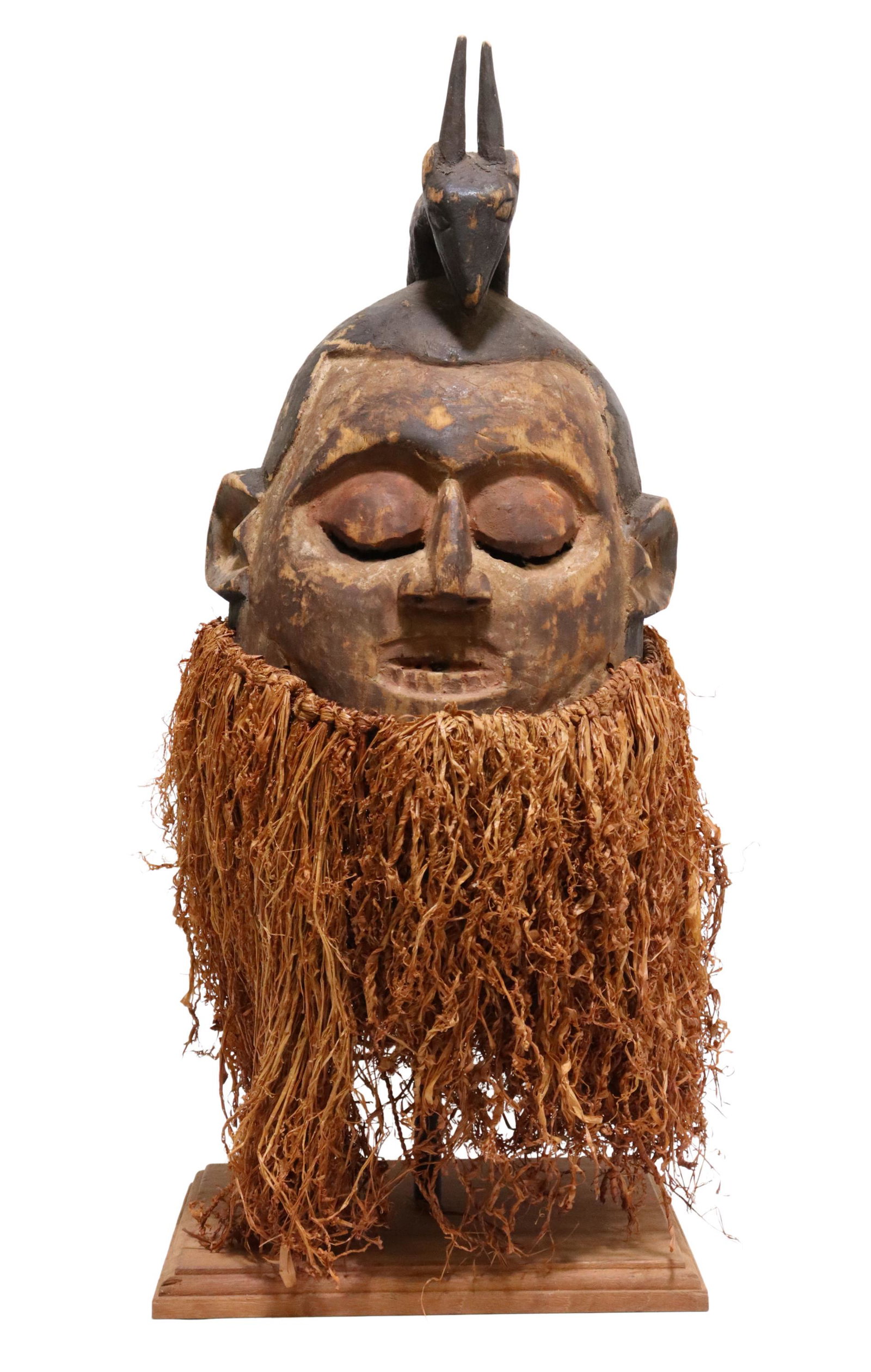 AFRICAN TRIBAL CARVED HEMBA HELMET MASK, SUKU: African tribal carved Hemba helmet mask, the Suku peoples, Democratic Republic of the Congo, animal totem, over round face, with incised teeth, remnants of pigment, raffia fringe, accompanied by stand