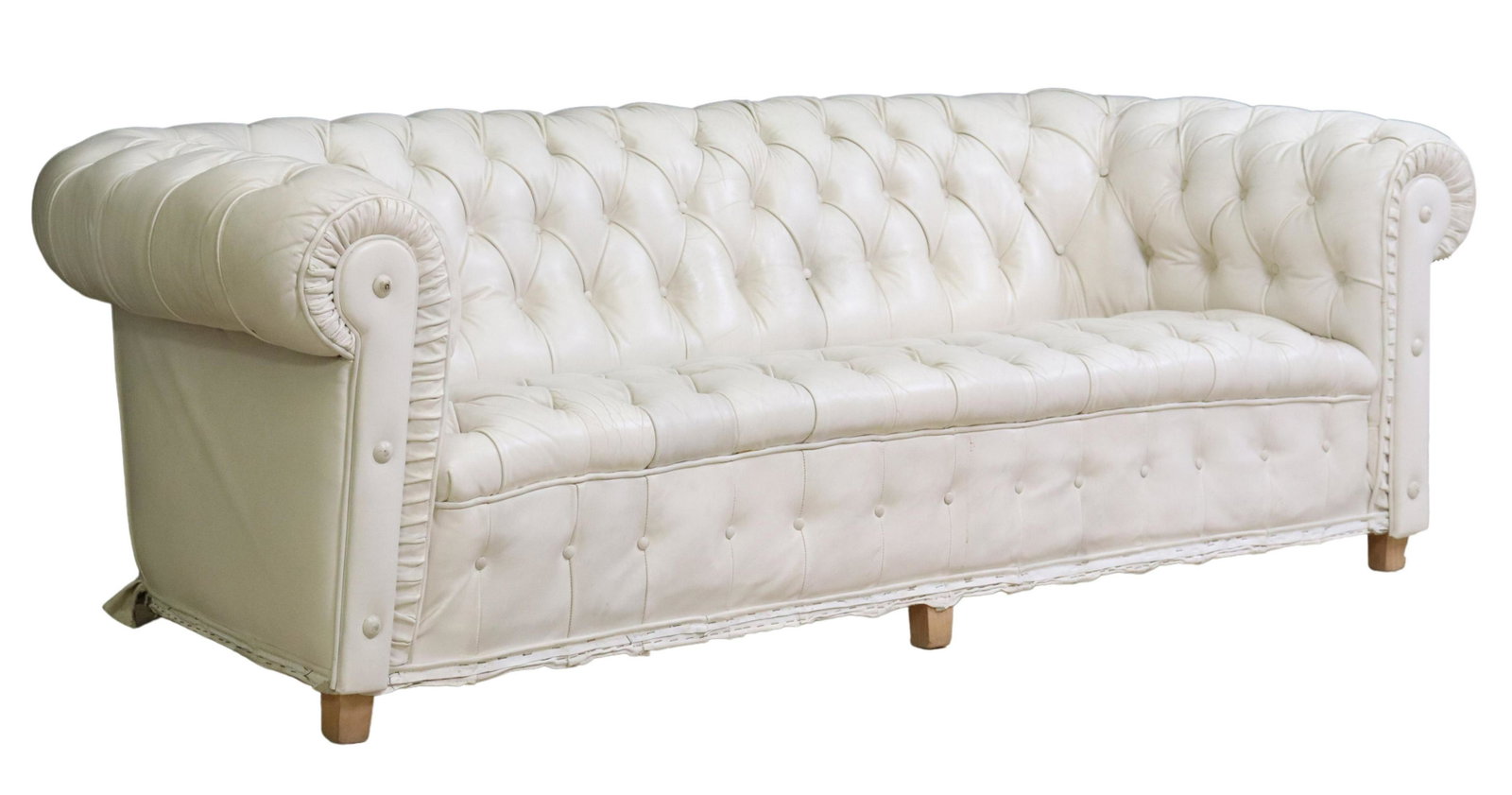 TUFTED WHITE LEATHER CHESTERFIELD STYLE SOFA: Chesterfield style sofa, 20th c., in worn white leather upholstery, with button-tufted rolled back and arms, partial ruffled skirt concealing block feet, as pictured, worn condition with button loss, 