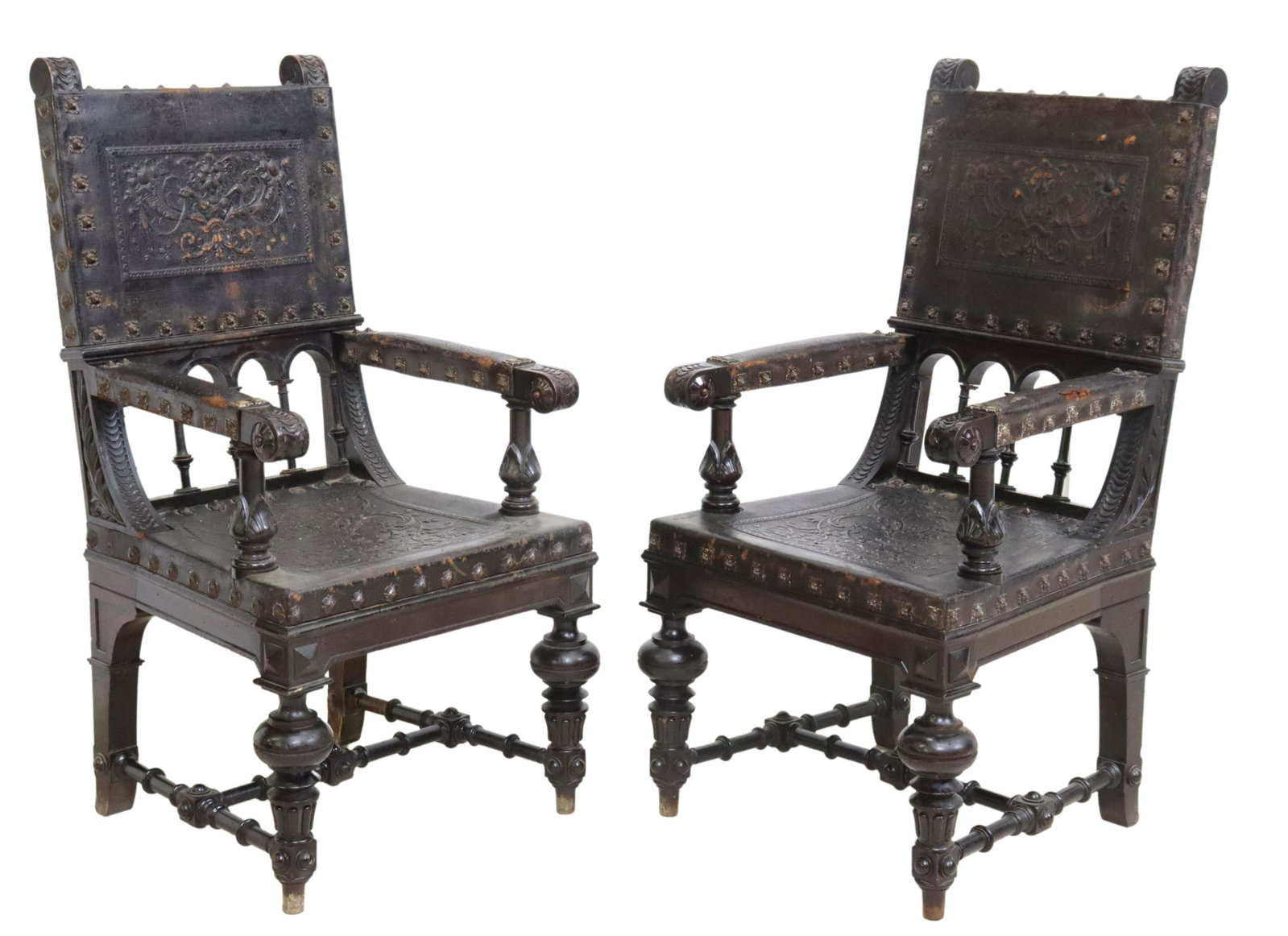 (2) SPANISH RENAISSANCE REVIVAL LEATHER ARMCHAIRS: (pair) Spanish Renaissance Revival carved armchairs, late 19th c., having embossed leather back and seat sling, with central lion masks flanked by scrolled foliates and fruit motifs, large nailhead tr