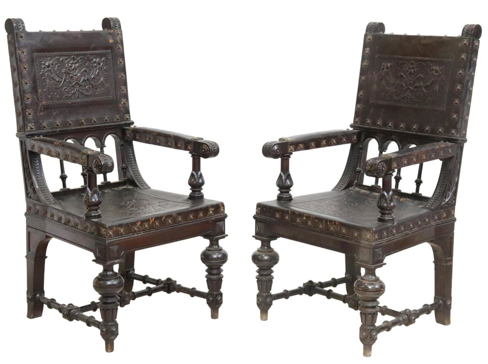 (2) SPANISH RENAISSANCE REVIVAL LEATHER ARMCHAIRS: (pair) Spanish Renaissance Revival carved wood armchairs, late 19th c., having embossed leather back and seat sling, with central lion masks flanked by scrolled foliates and fruit motifs, large nailhe