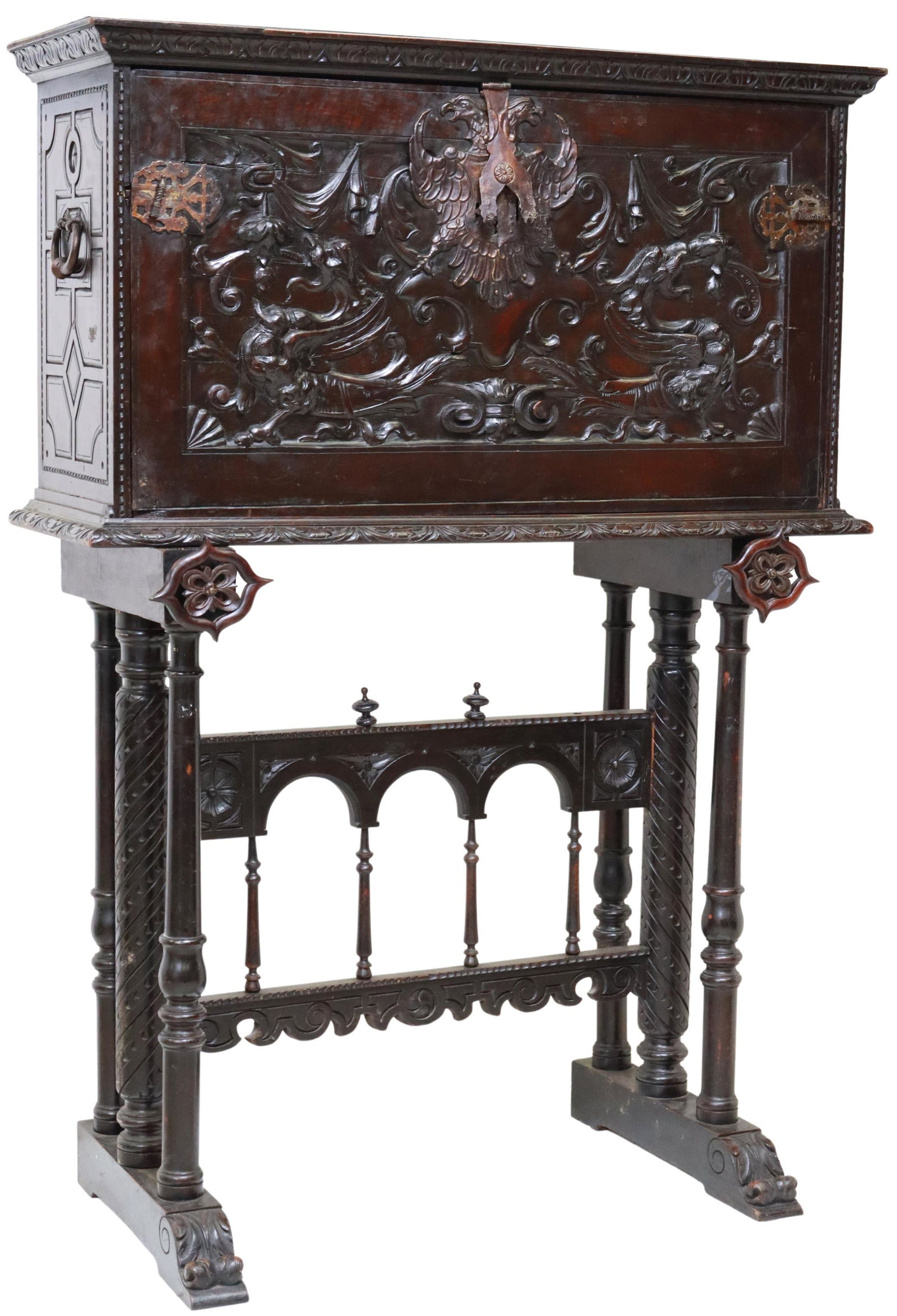 SPANISH RENAISSANCE REVIVAL VARGUENO ON STAND: Spanish Renaissance Revival bargueno/ vargueno on stand, early 20th c., having foliate trim, over fall front carved with double-headed eagle and dragons, opening to interior gallery, iron side handles