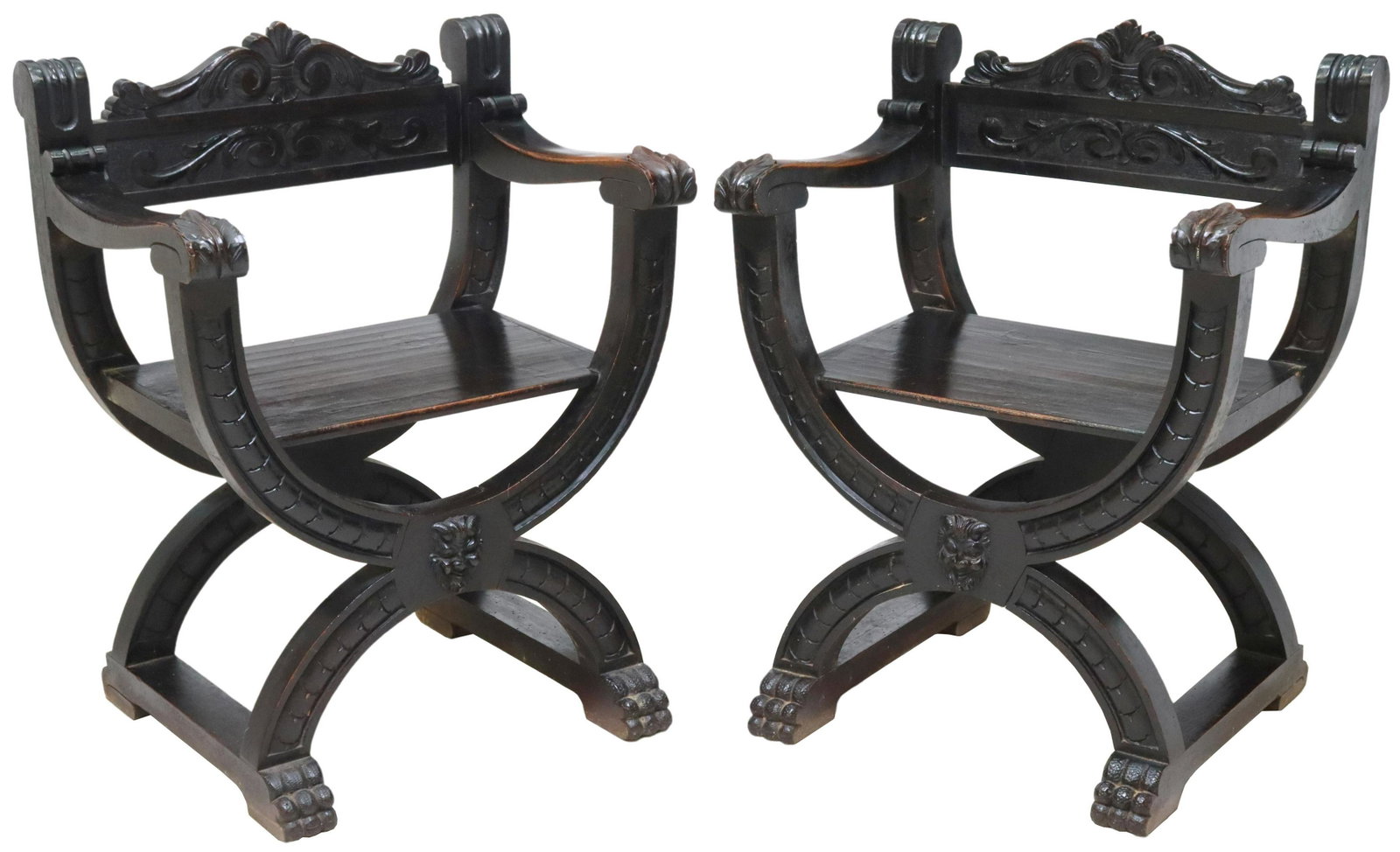 (2) SPANISH RENAISSANCE REVIVAL CURULE CHAIRS: (pair) Spanish Renaissance Revival ebonized chairs, 19th c., having carved foliate crest, scrolled handholds, grotesque mask apron, rising on curule base, ending in paw feet, approx 33.5"h, 25.25"w, 1