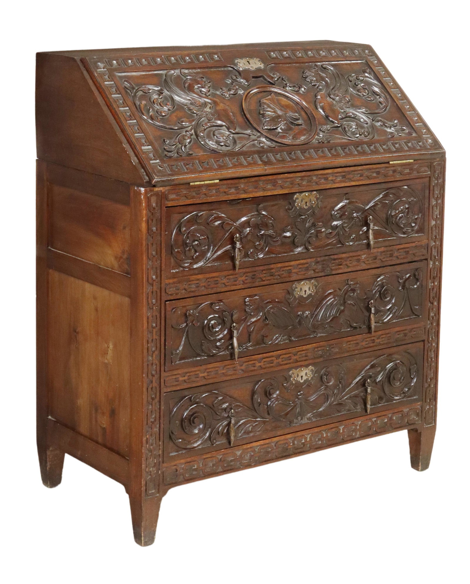 SPANISH RENAISSANCE REVIVAL SLANT-FRONT DESK: Spanish Renaissance Revival walnut desk, early 20th c., slant-front panel carved with knight profile medallion, grotesques, opening to interior gallery with two small cabinets, over three exterior dra