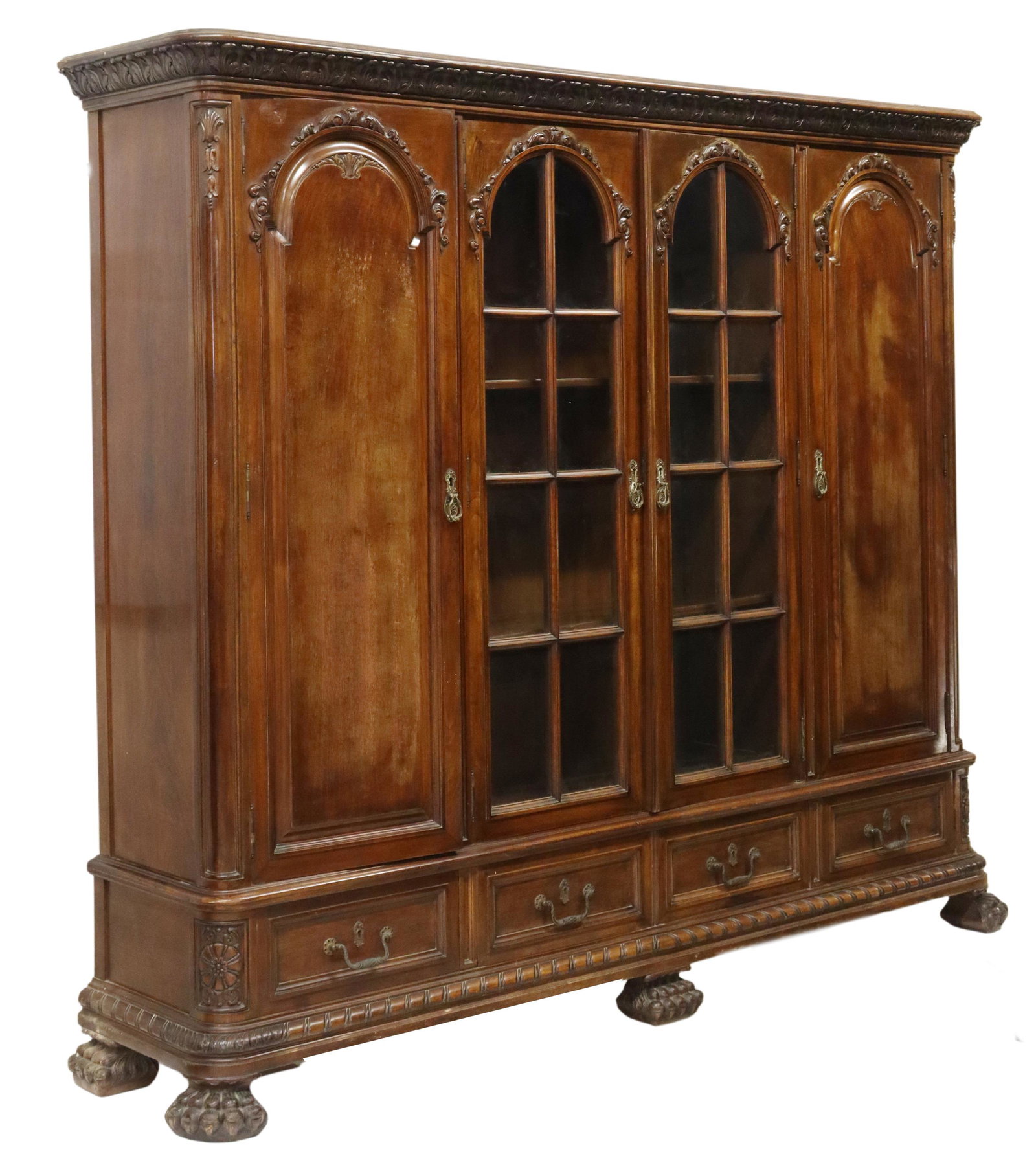 SPANISH CARVED LIBRARY BOOKCASE, 72"H: Spanish library bookcase, late 19th/early 20th c., having foliate cornice, over two glazed central doors, flanked by two side cabinets, all over four drawers, ending on paw feet, flaking to varnish at