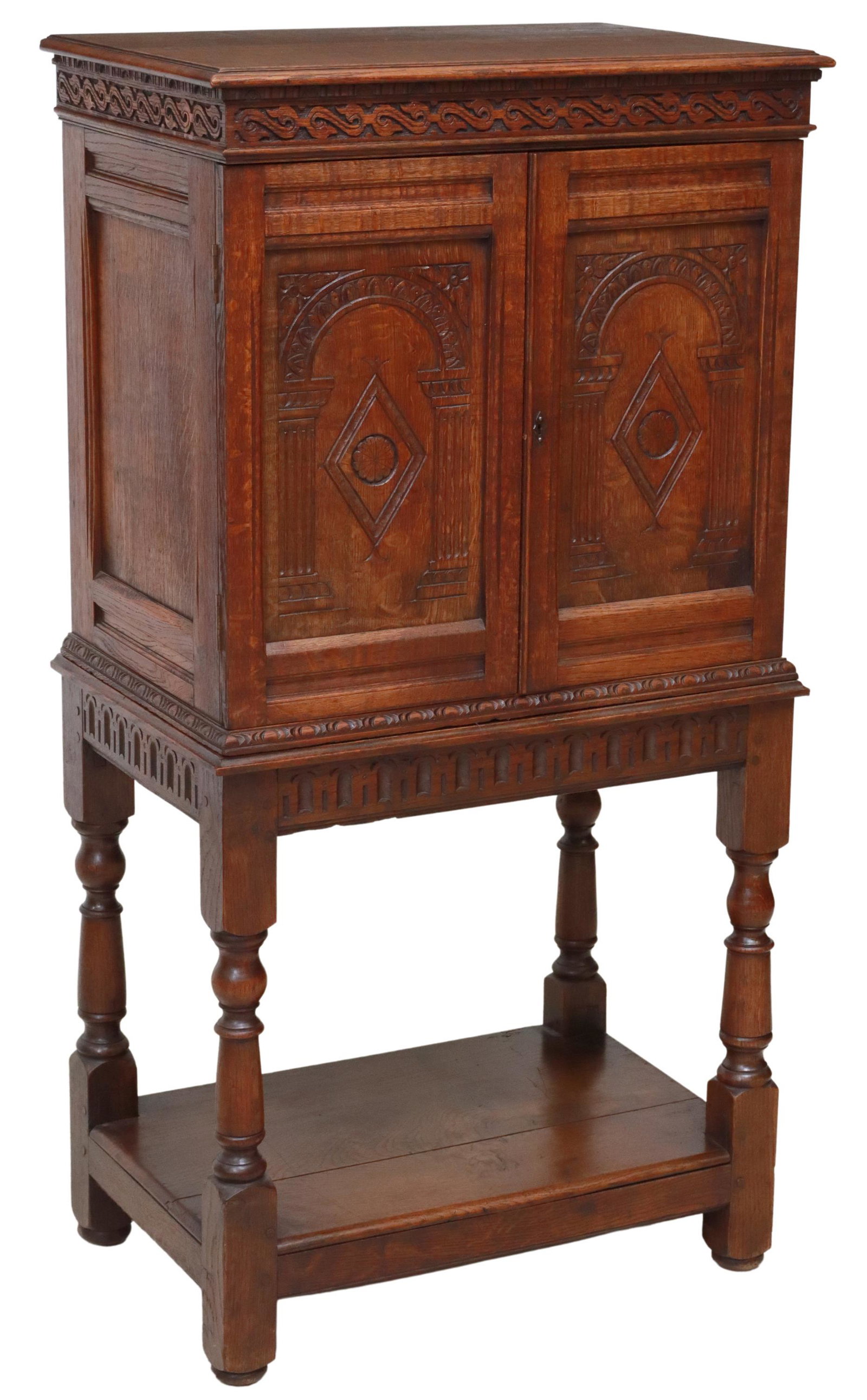 ENGLISH JACOBEAN STYLE OAK CABINET ON STAND: English Jacobean style oak cabinet on stand, late 19th c., having carved foliate border, over two paneled and arcaded doors, opening to twelve drawers in varied sizes, rising on turned legs, above ope