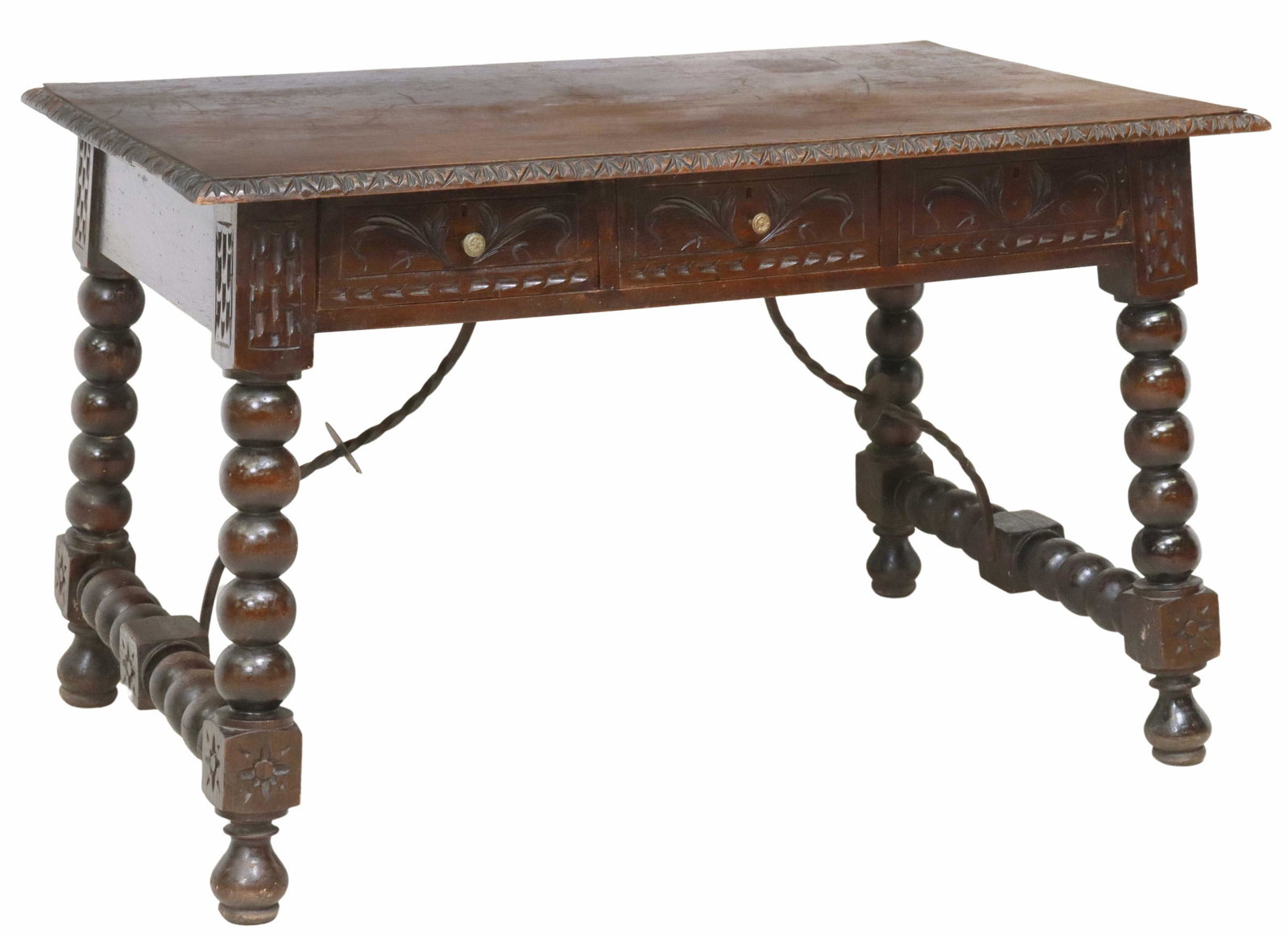 SPANISH BAROQUE STYLE CARVED LIBRARY TABLE/ DESK: Spanish Baroque style library table/ desk, 19th c., carved foliate border, fitted with three drawers, rising on turned stretcher-joined legs, with iron cross stretcher, ending on bun feet, lacking one