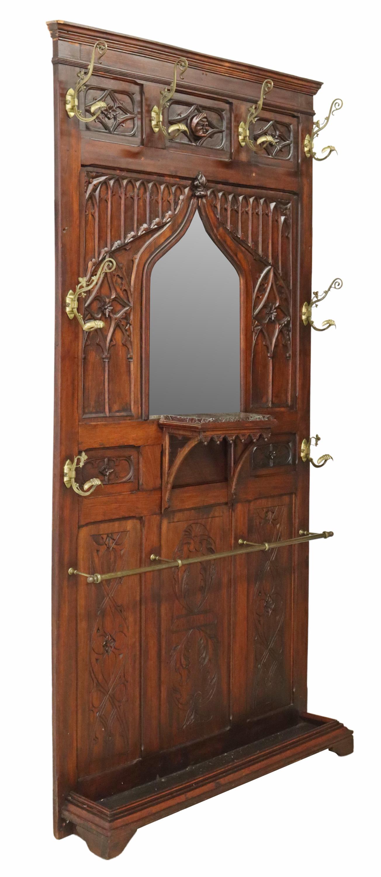 GOTHIC REVIVAL CARVED & MIRRORED HALL TREE: Gothic revival hall tree, 19th c., having molded cornice, over central protruding mask, tracery arcaded backboard, issuing eight gilt metal foliate hooks, ogee arch frame, encasing beveled mirror plat