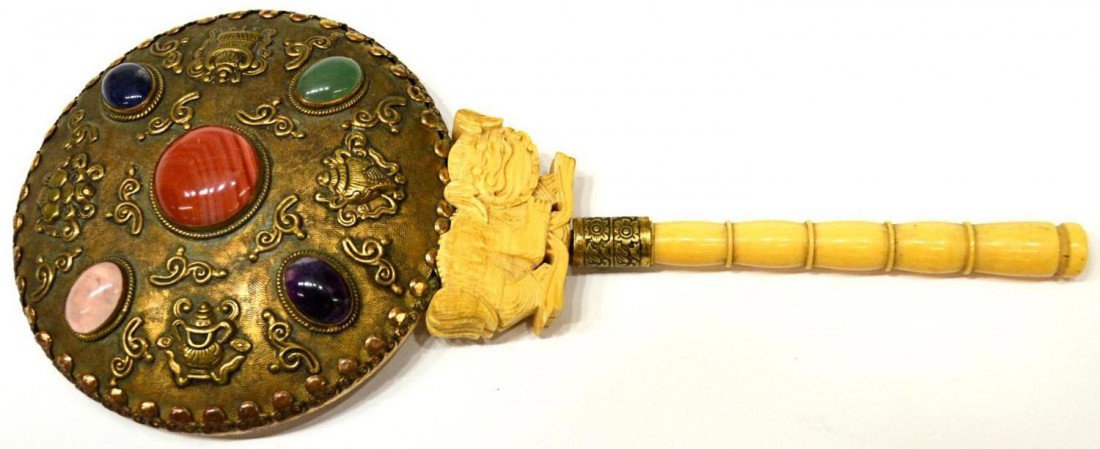 CHINESE HAND MIRROR, IVORY HANDLE & FOO DOG: Chinese hand mirror, early 20th c., the gilt metal mirror with foliated repousse decoration set with five stone cabochons, 2" wide ivory foo lion joining the patinated turned ivory handle, 9.5/8"l, 4.